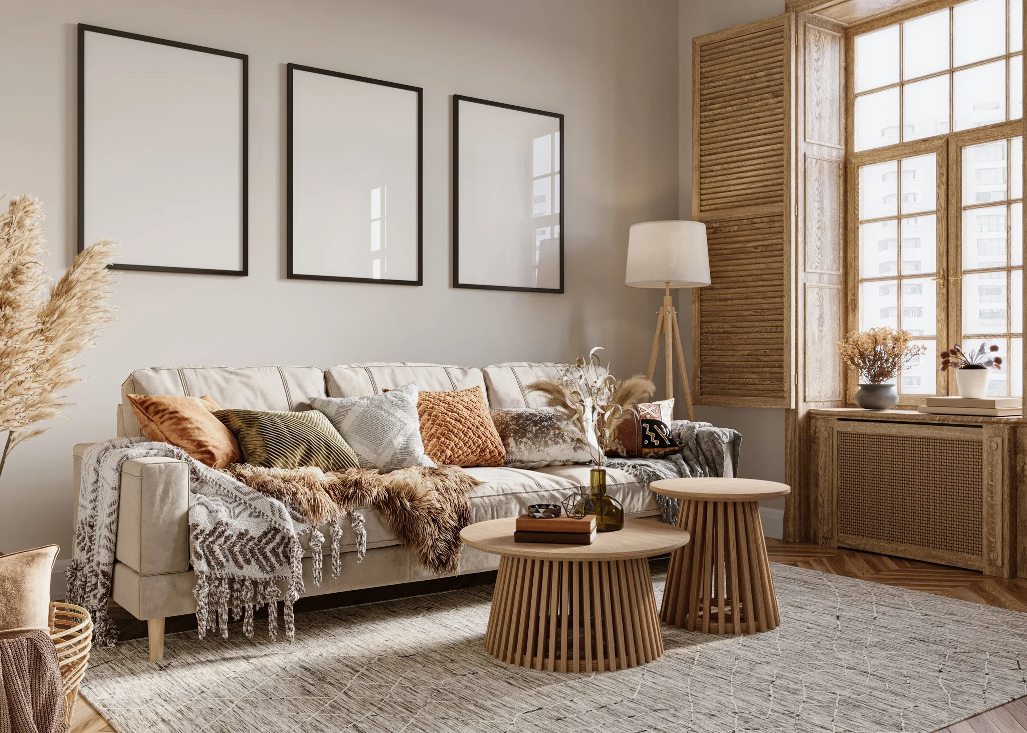 Living room with a beige sofa adorned with various textured pillows and a woven throw. Two round wooden coffee tables are in front, with decorative items including books and a vase with dried flowers. The room features a large window with wooden shutters, a tall floor lamp, and wall art with three empty rectangular frames. The decor has neutral tones and natural materials, creating a cozy and modern ambiance.