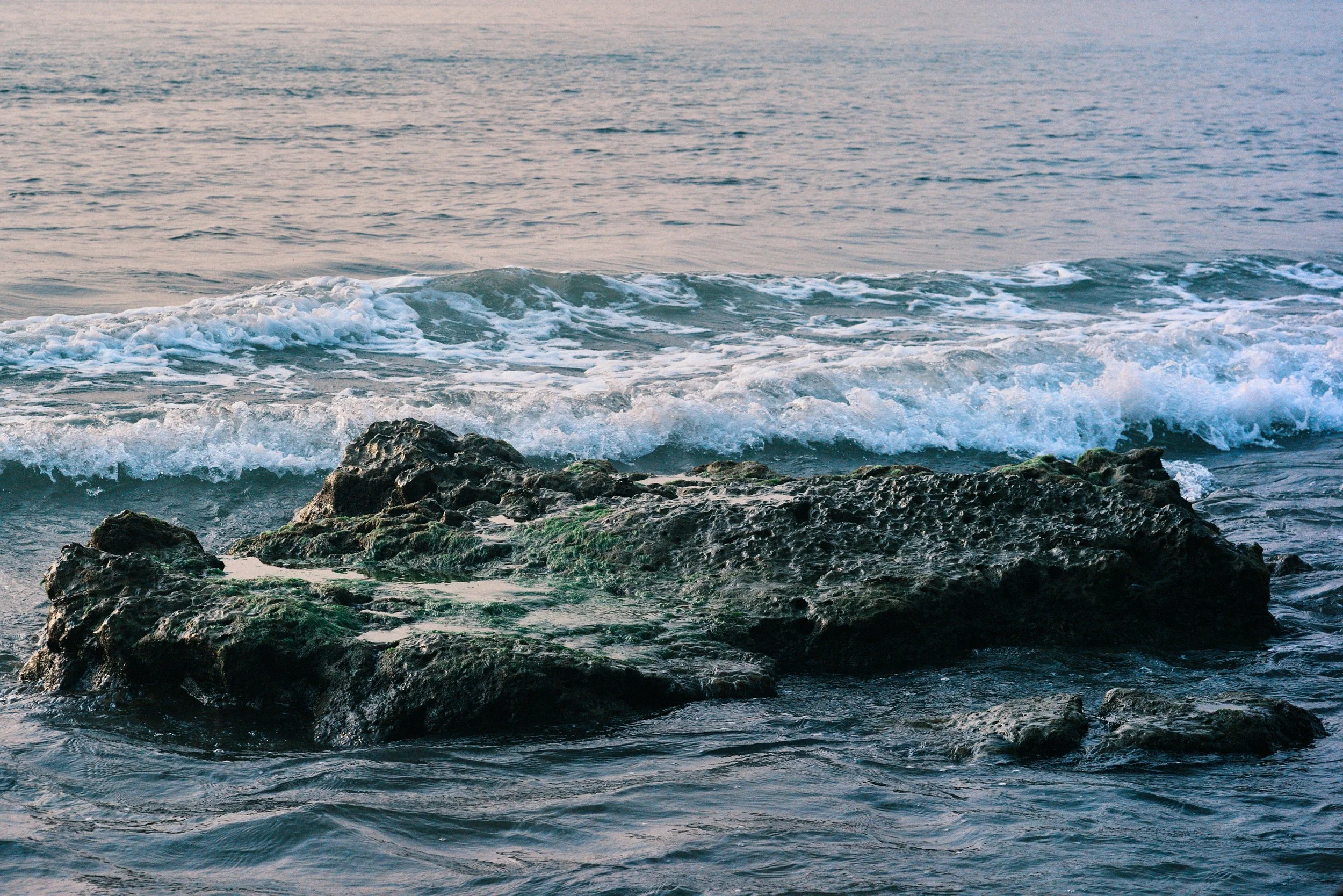 Photo of ocean waves crashing against rocks during sunset.