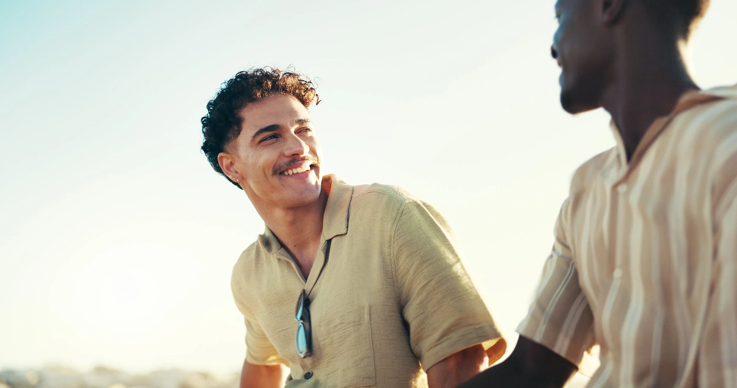 Two men sitting outdoors, smiling and engaging in conversation during a sunny day.