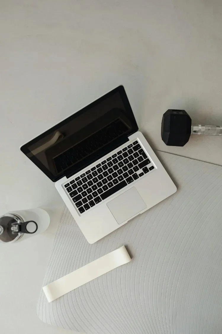 Laptop, water bottle, and fitness equipment arranged on a clean workspace, representing online health coaching and virtual movement sessions offered from Henderson, Nevada to clients worldwide.