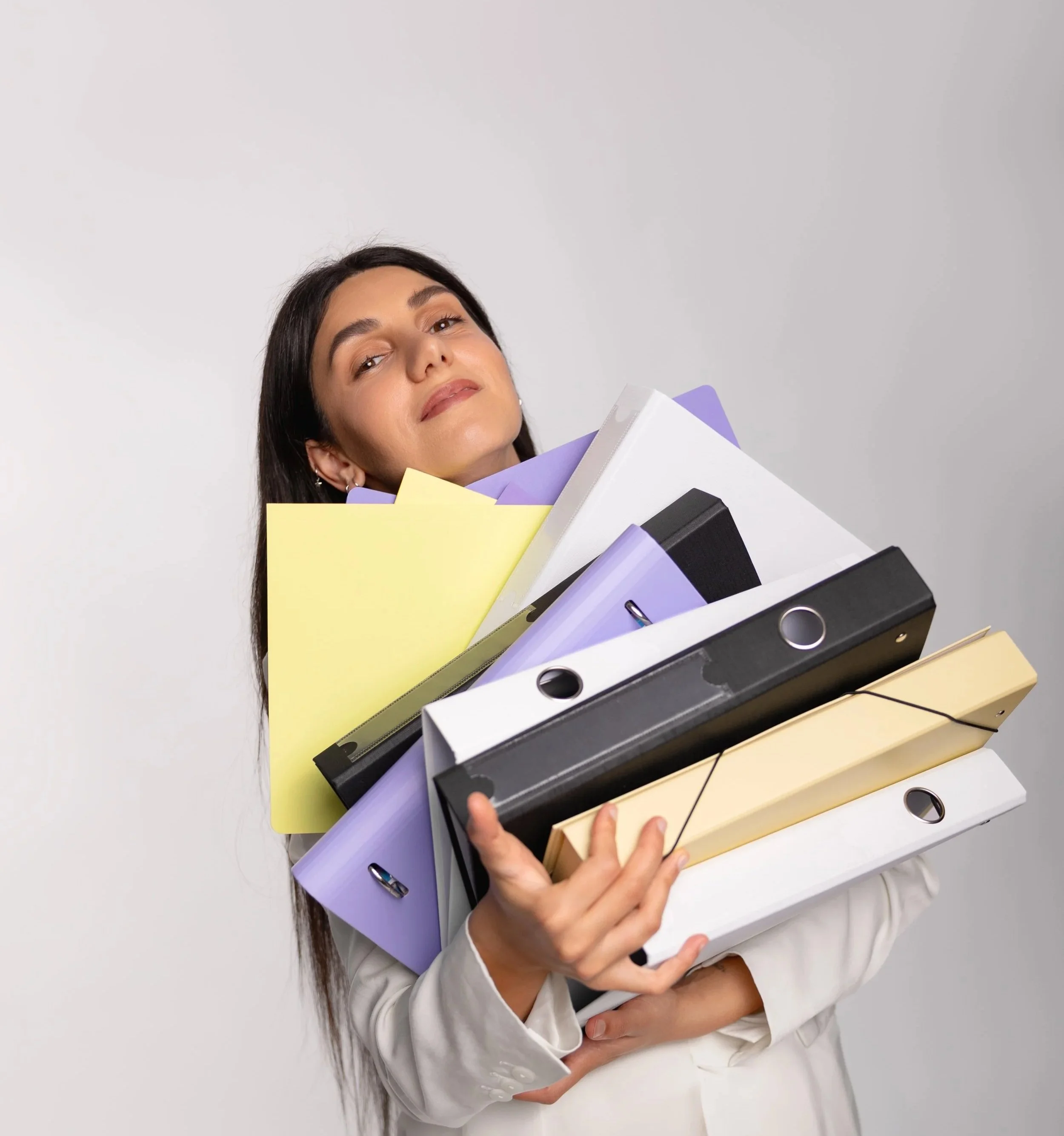 Person holding multiple colorful binders and folders against a plain gray wall.
