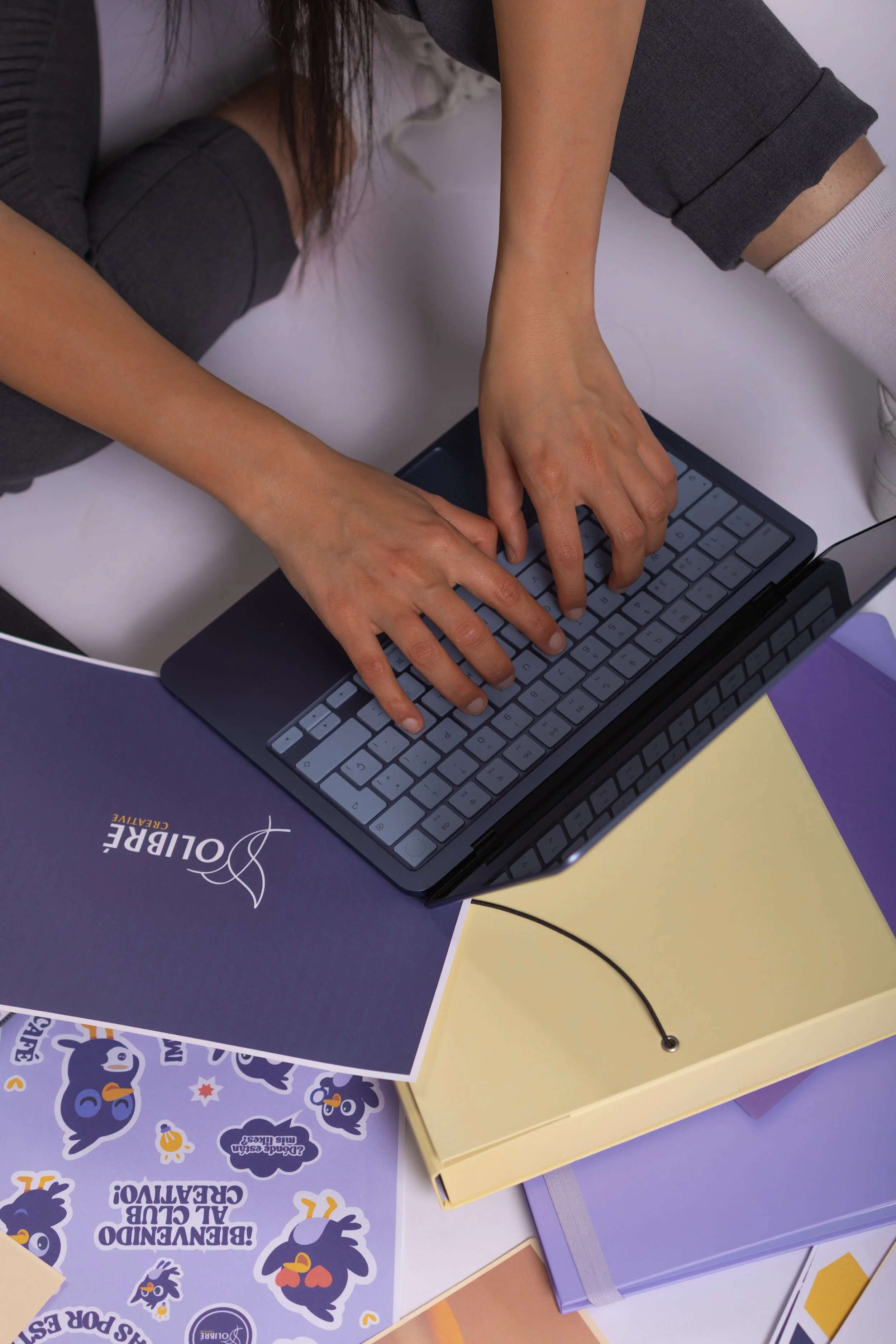 An electronic keyboard on a desk surrounded by colorful notebooks and posters, with some documents and a cable visible.