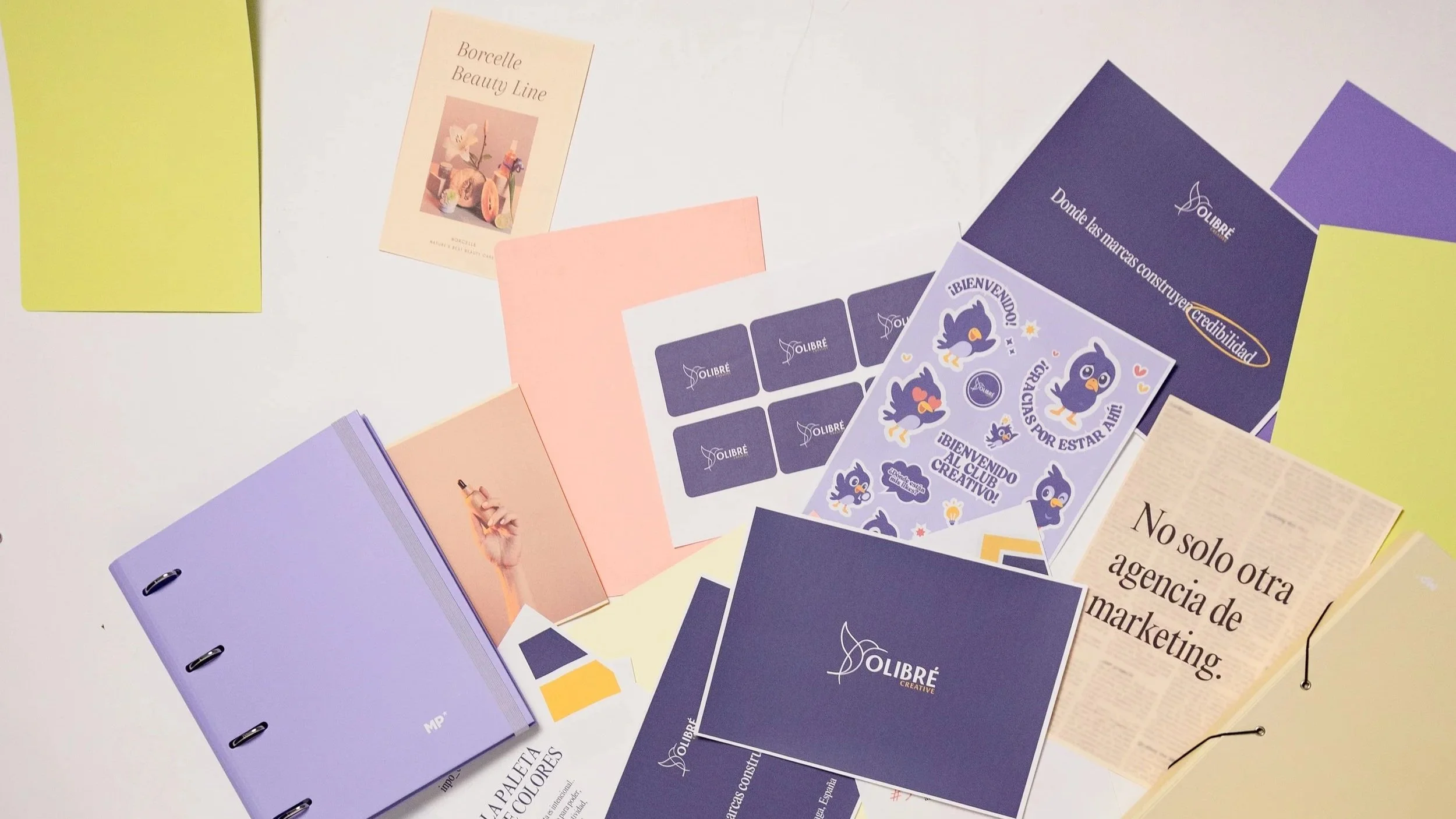 Various colorful brochures, notebooks, and flyers spread out on a white surface, some featuring branding and graphics related to a creative or marketing agency.