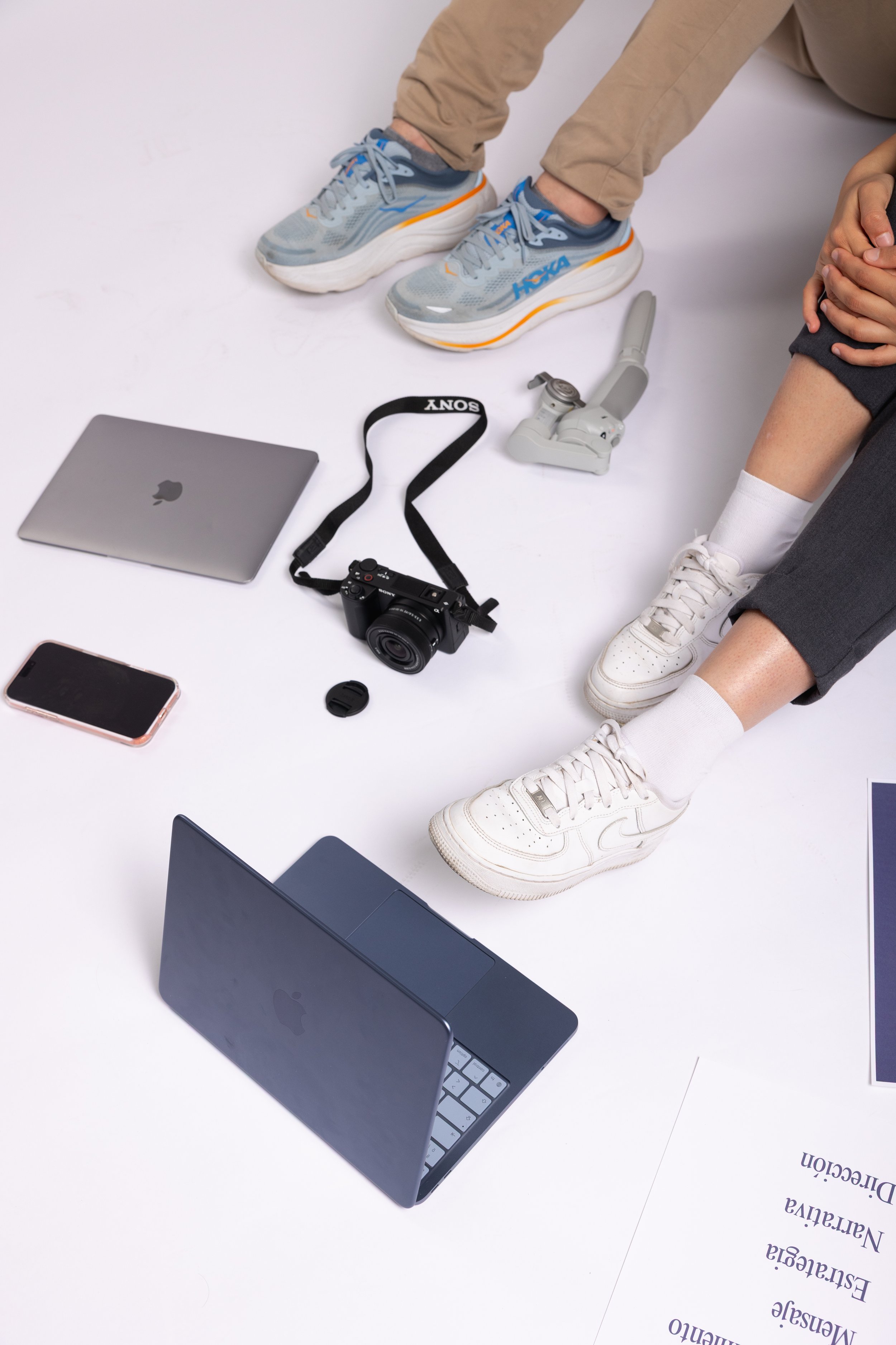 People sitting on the floor, with a laptop, smartphone, camera, and other electronic devices spread around them.