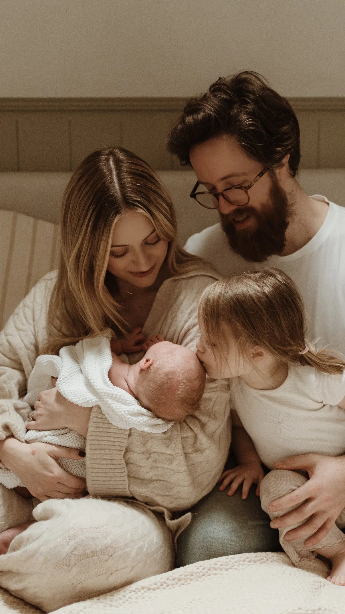 A family of five with three children, a mother, father, and two girls, gathered around a newborn baby for a tender moment in a cozy, warmly lit room.