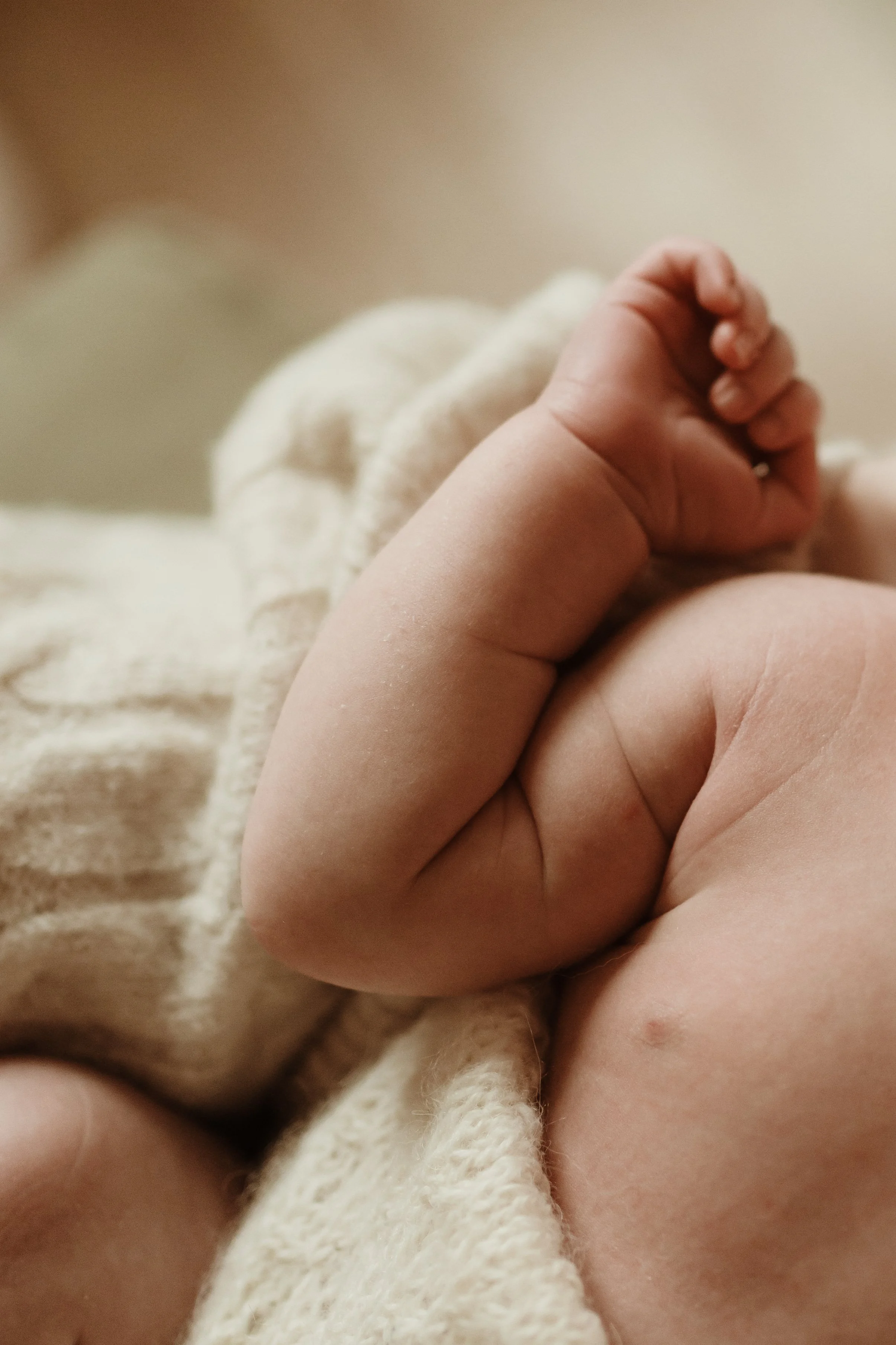 Close-up of a baby's hand gripping an adult's finger, with soft beige and white clothing in the background.