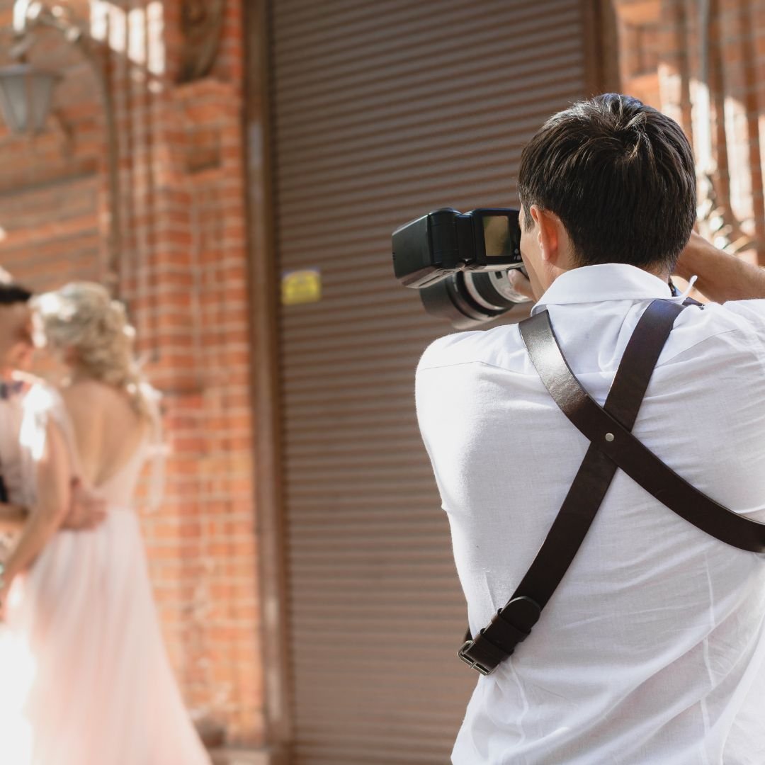 Photographer taking a photo of a wedding couple in front of a brick building.