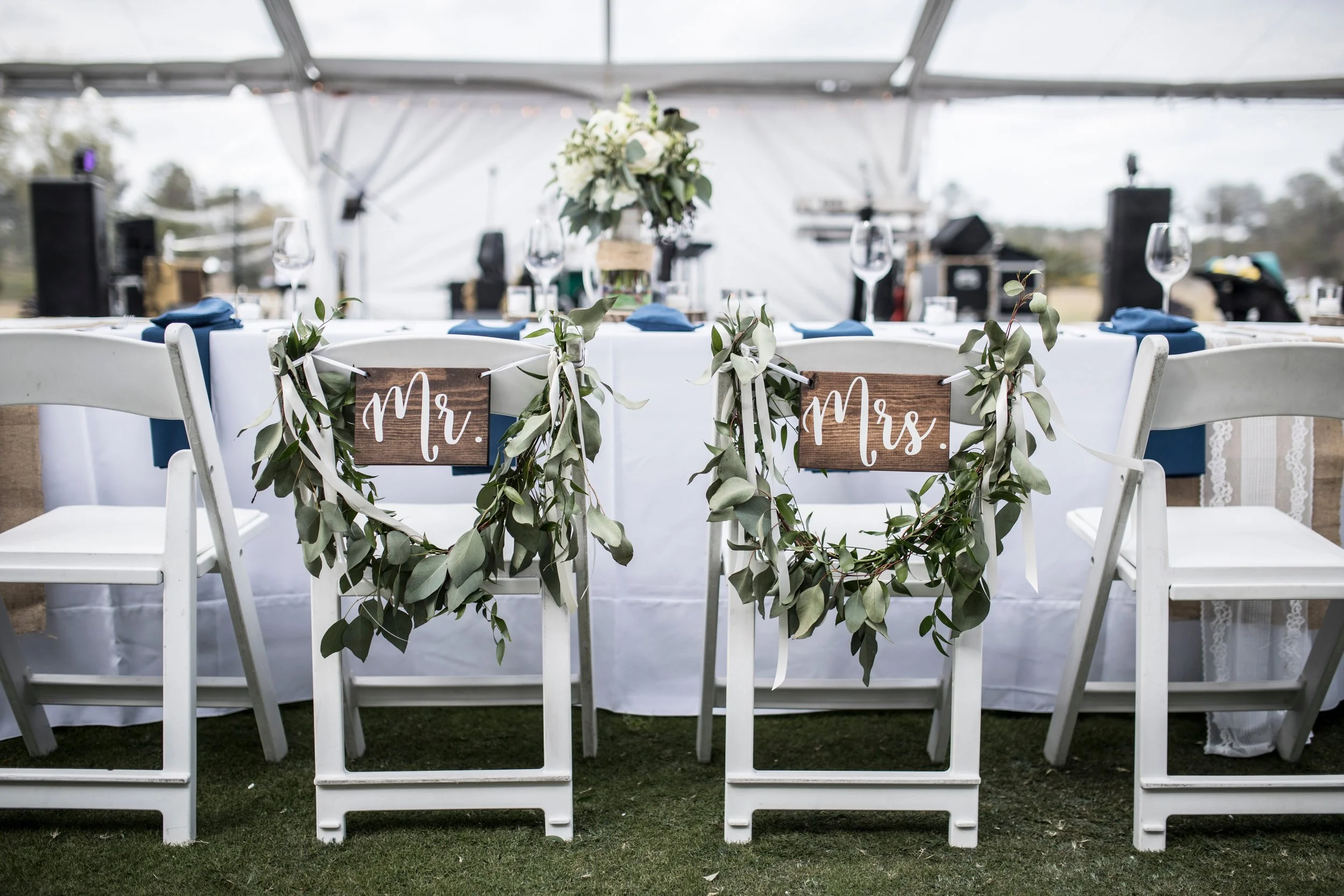 Wedding reception table with Mr. and Mrs. signs on chairs decorated with greenery garlands.