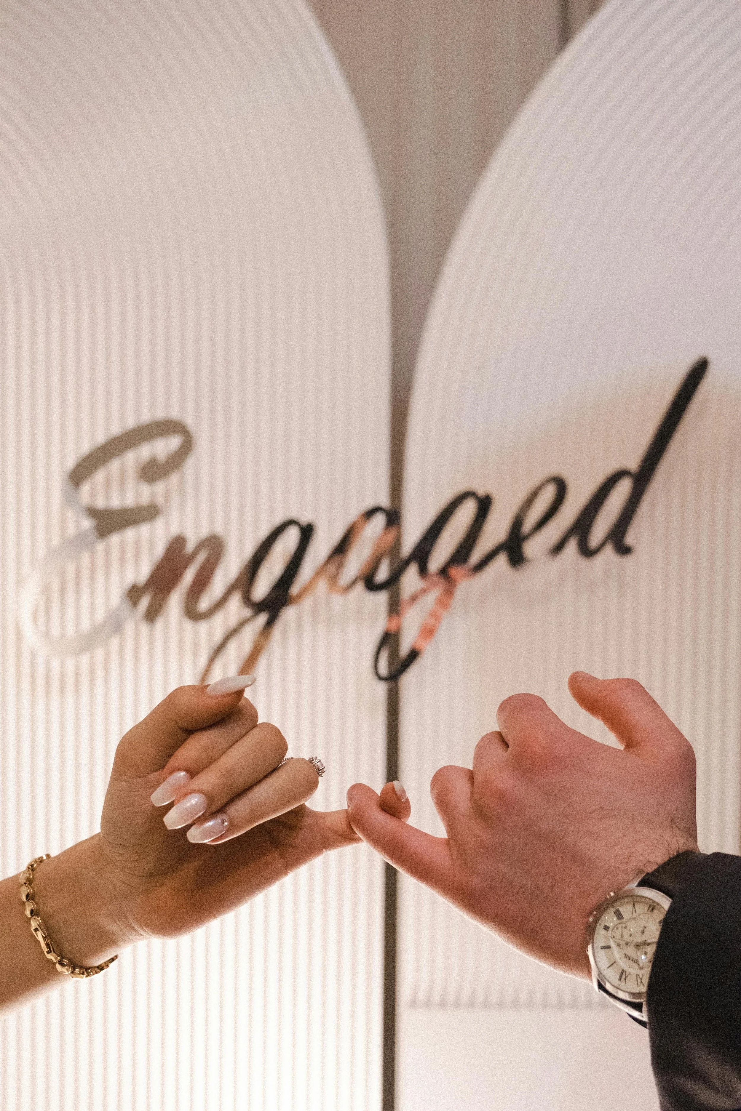 Close-up of a man and woman holding a wedding ring near a sign that says 'engaged' in a modern setting.