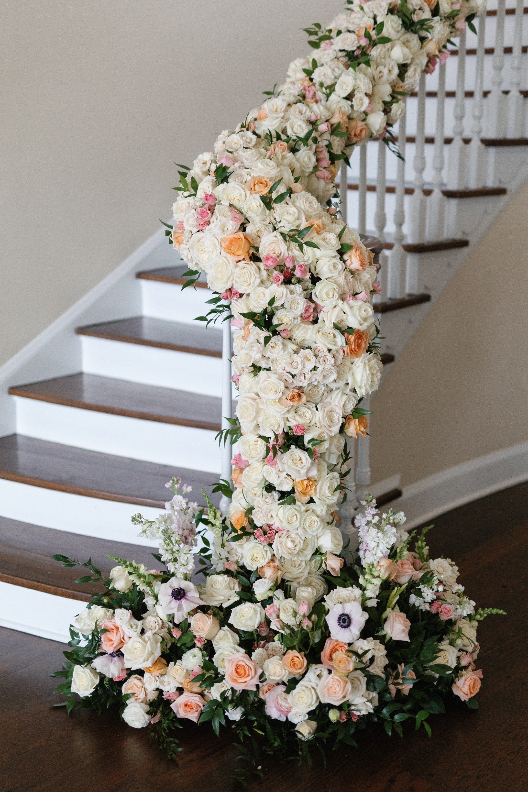 A floral arrangement with white, pink, and peach roses, along with other flowers and greenery, decorating a staircase railing.