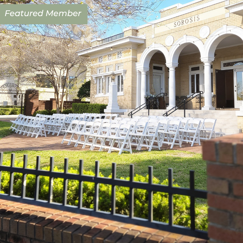 Elegant banquet hall decorated for a formal event with round tables covered in black tablecloths, adorned with white floral centerpieces, surrounded by gold chiavari chairs with white cushions, and decorated with glassware, napkins, and silverware.