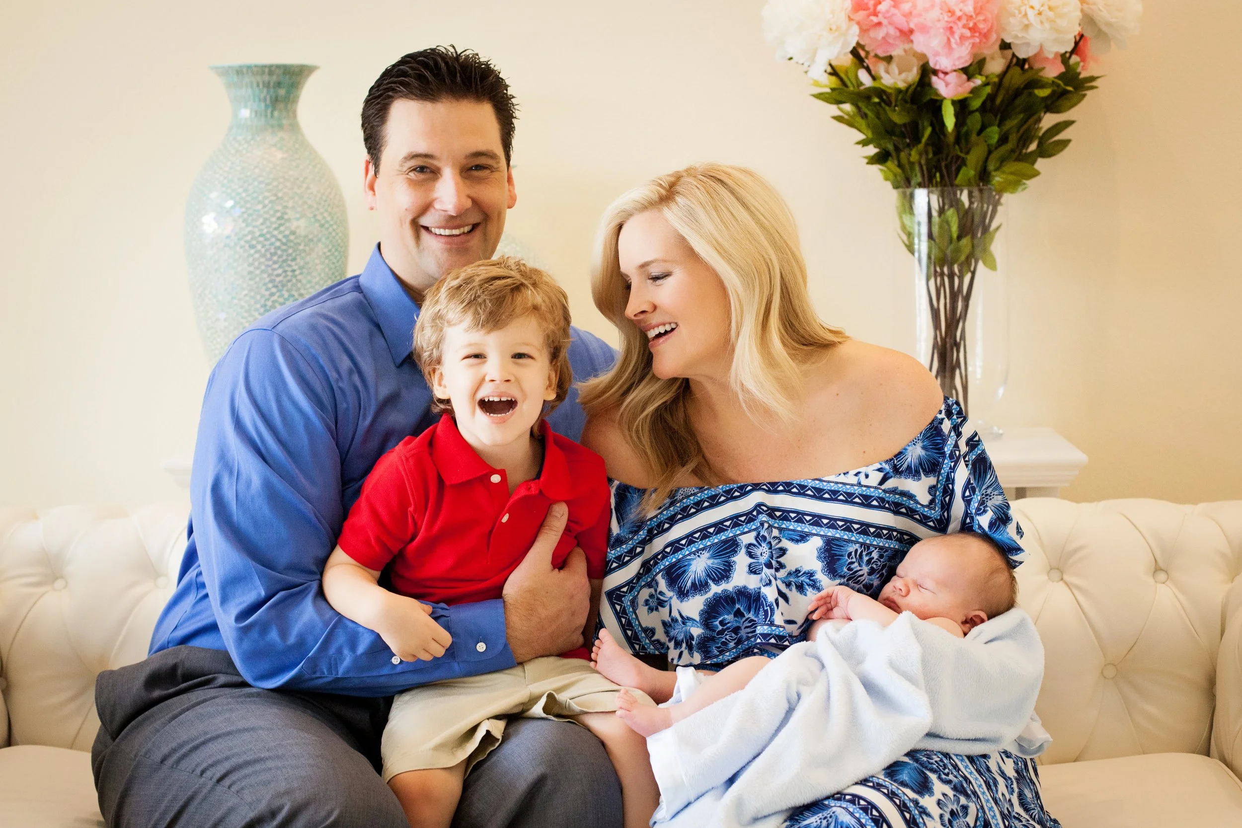 In-home newborn family photography of parents and children gathered on a sofa admiring their newborn