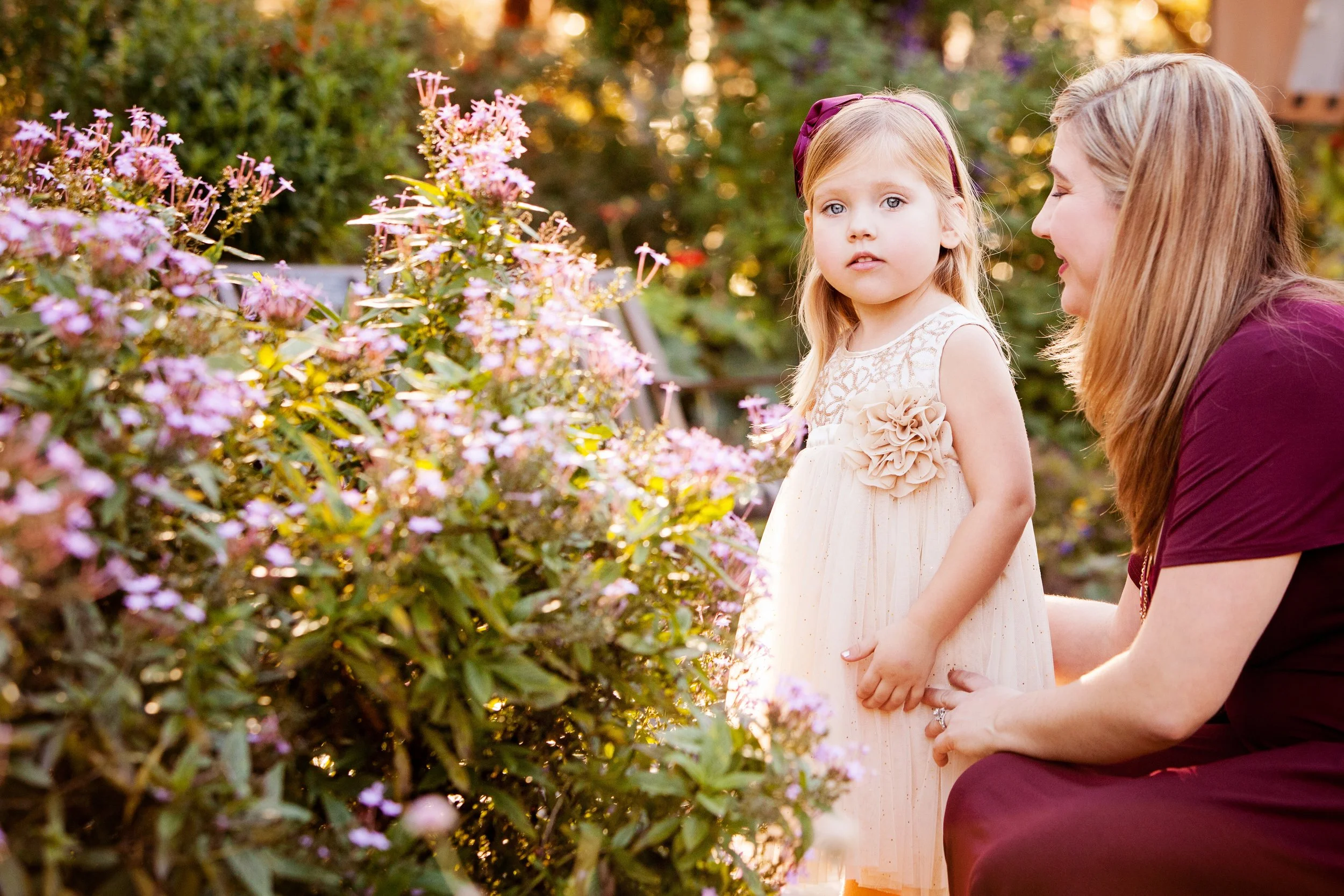 Mother-daughter lifestyle portrait near blooming flowers during golden hour