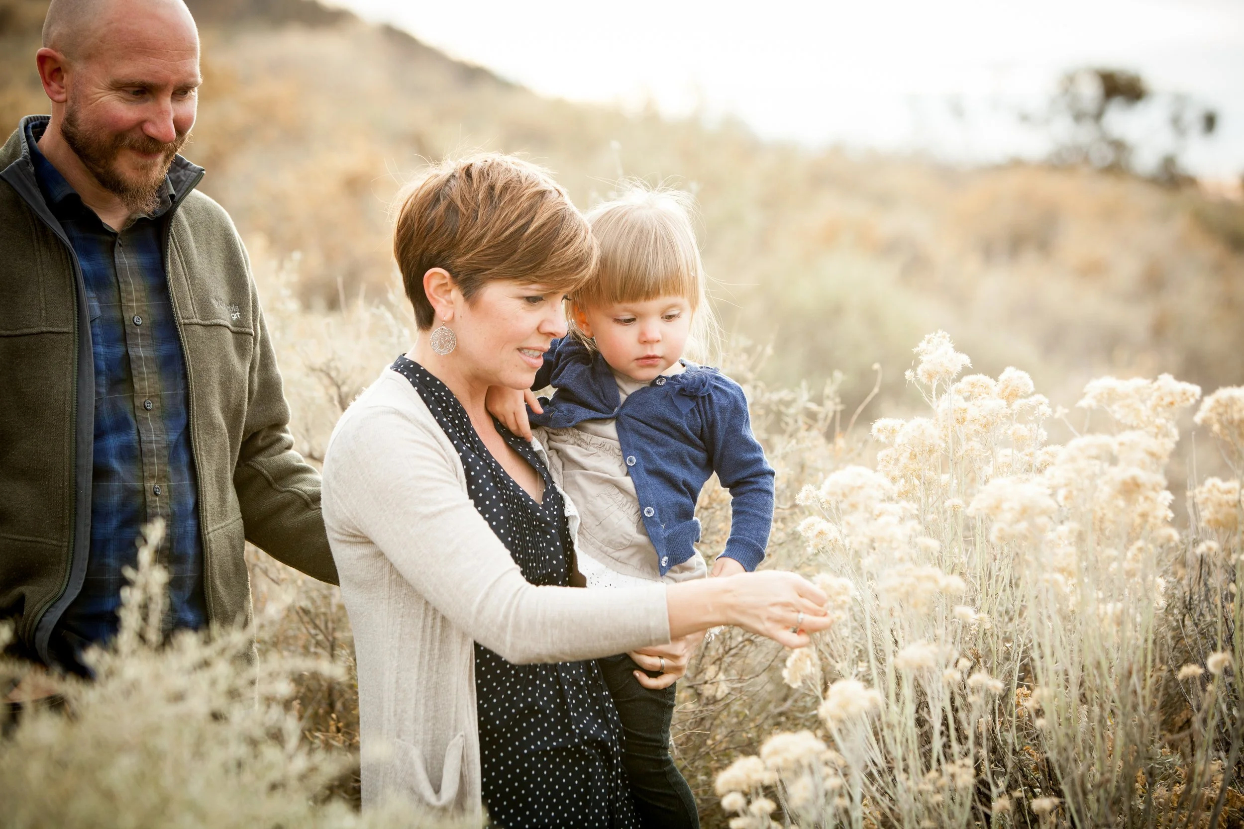 Autumn family photography of parents walking with their young daughter through wildflowers in Florida.