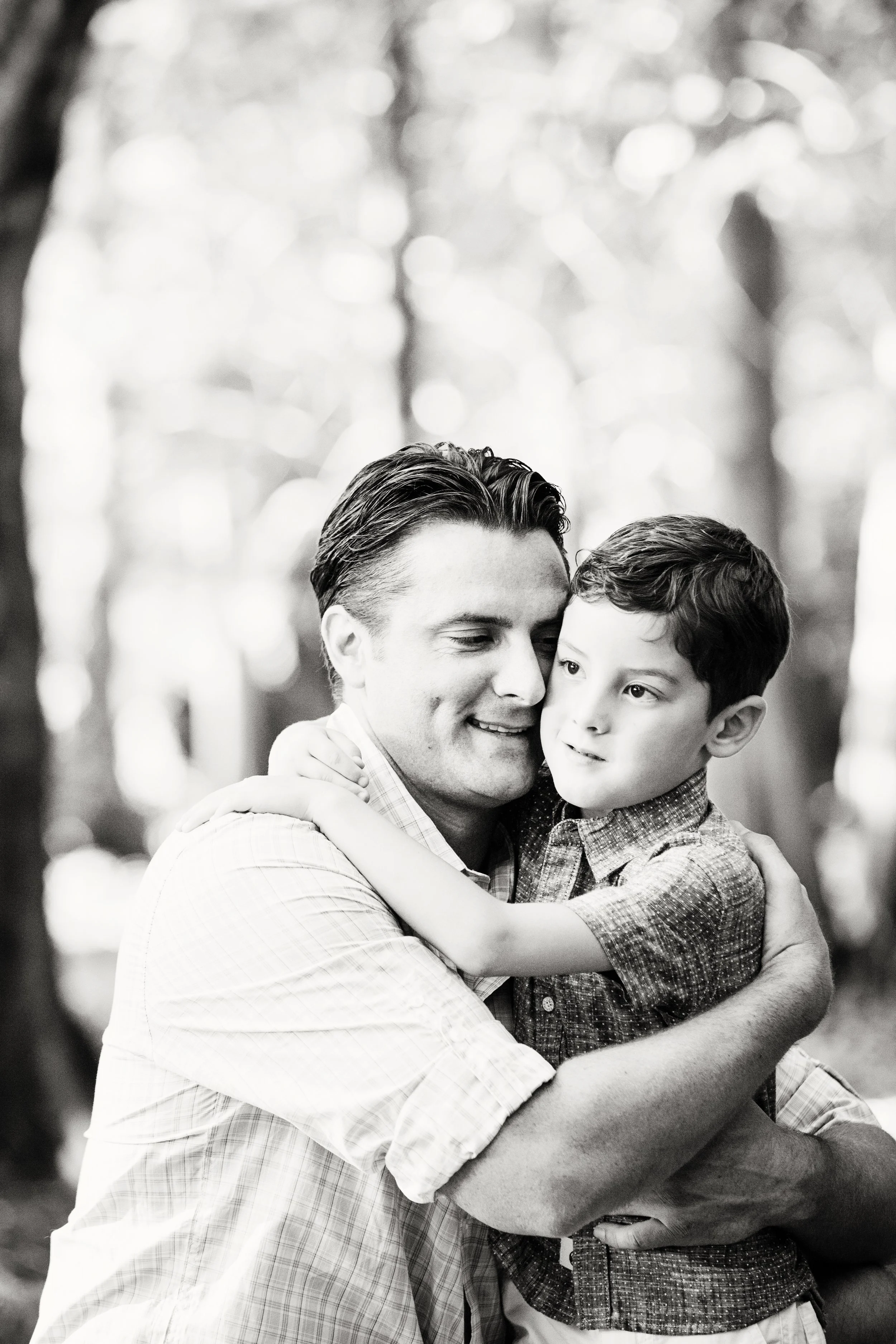 Lifestyle family photography of a father hugging his young son outdoors beneath trees