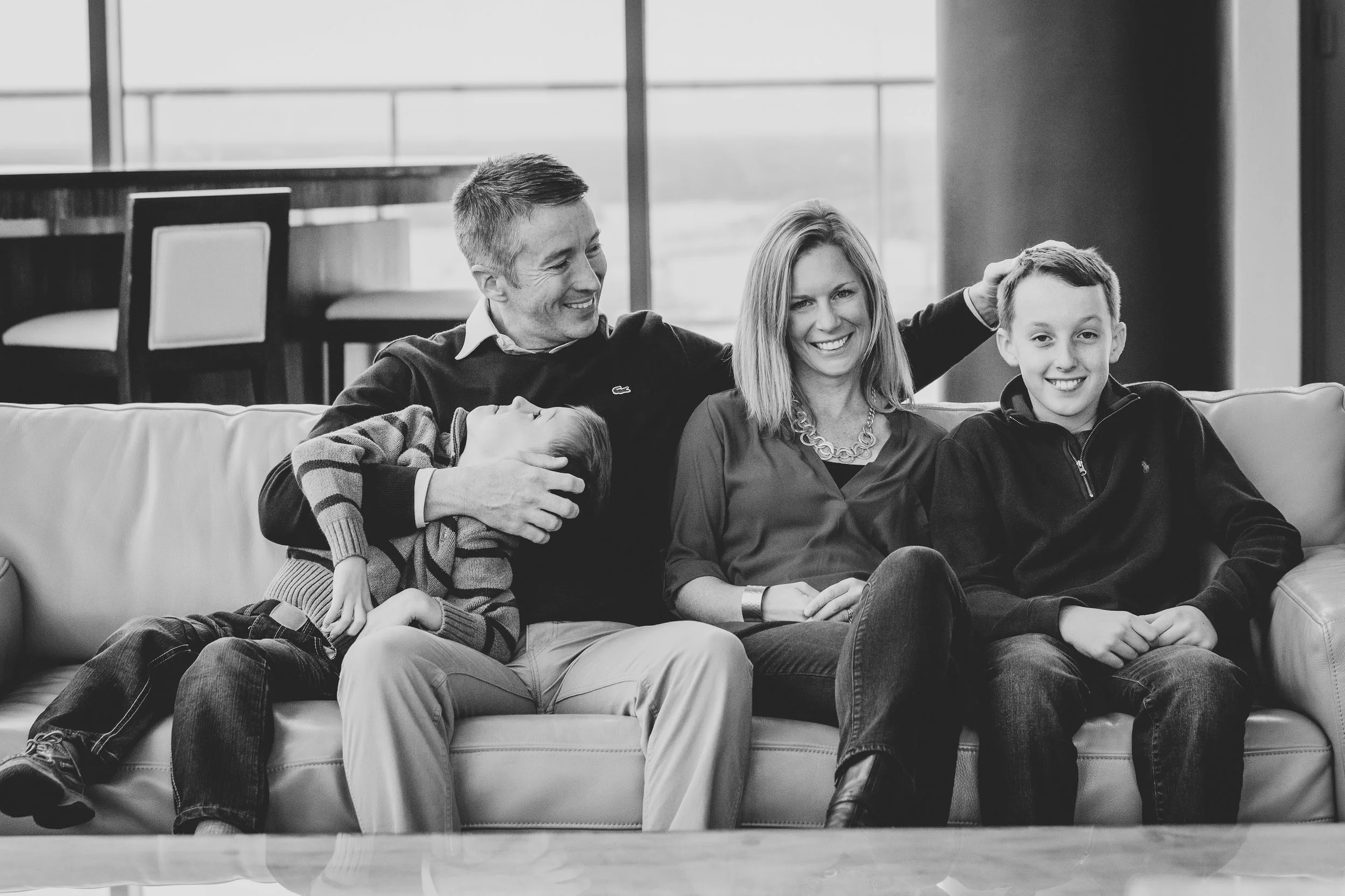 Black and white lifestyle family photography of parents and children laughing together on a couch