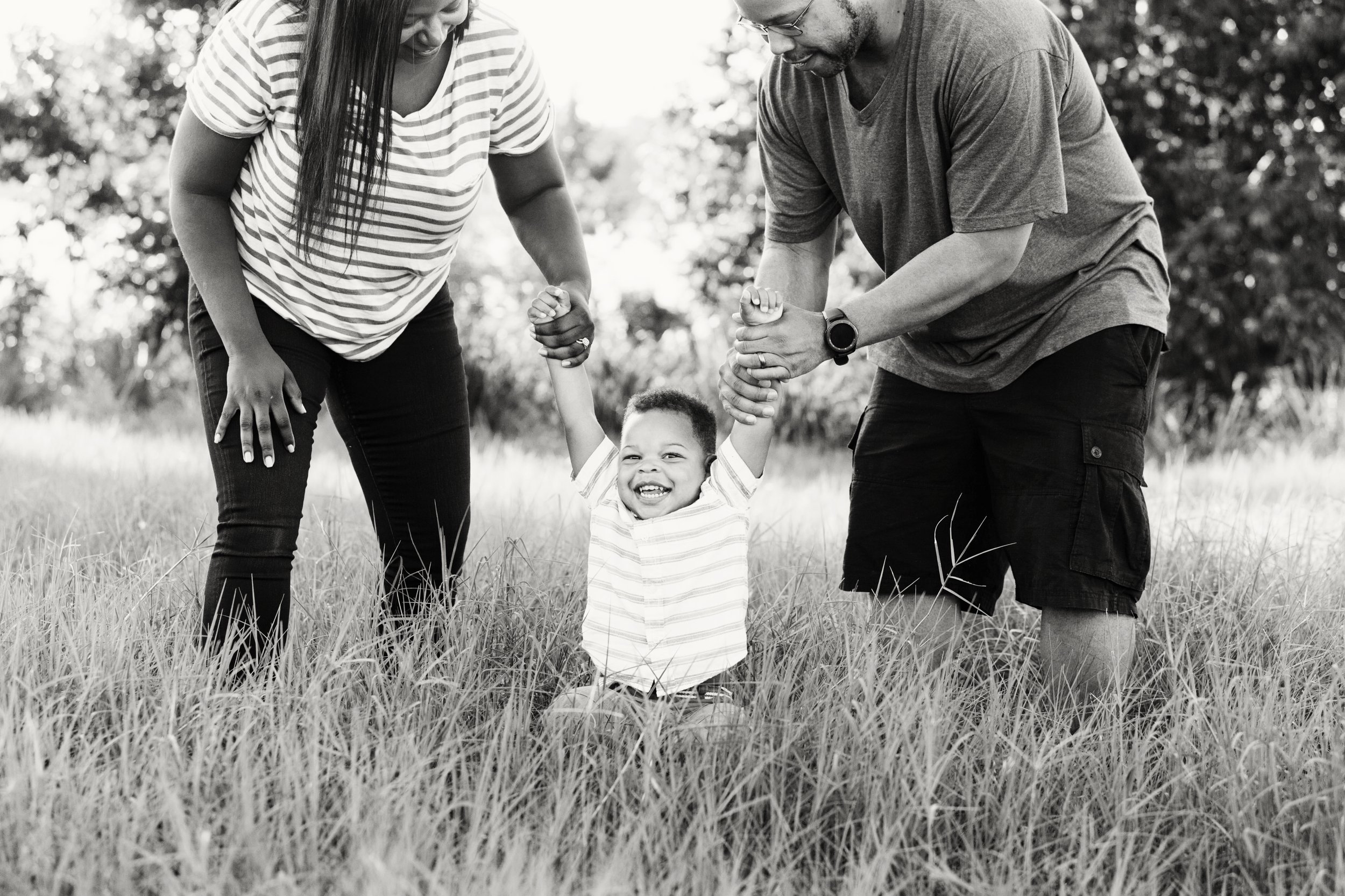 Lifestyle family portrait of parents supporting their young son as he stands in a grassy field
