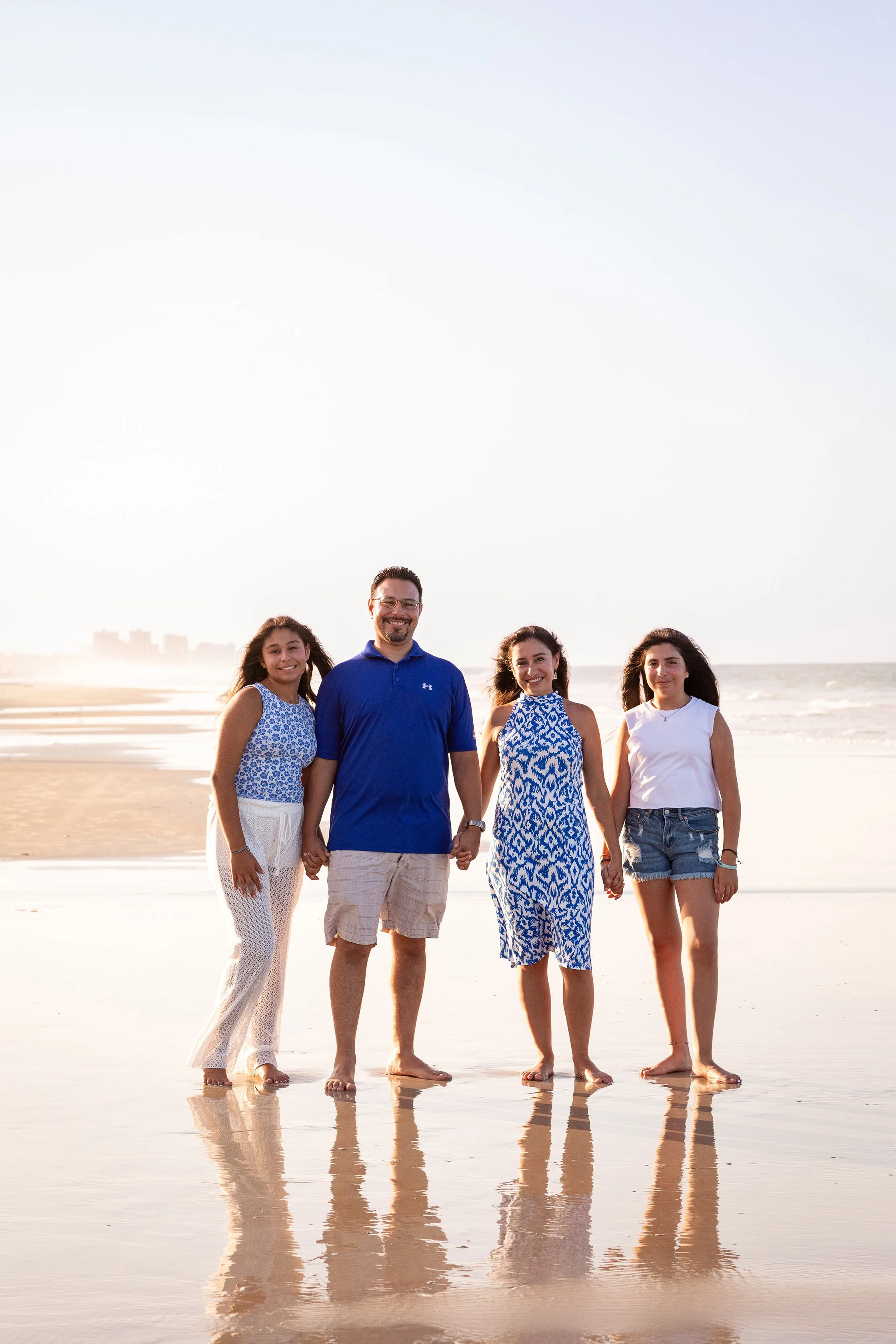 Beach family photography of a family of five holding hands at sunset, on a Florida shoreline with ocean waves in the background.