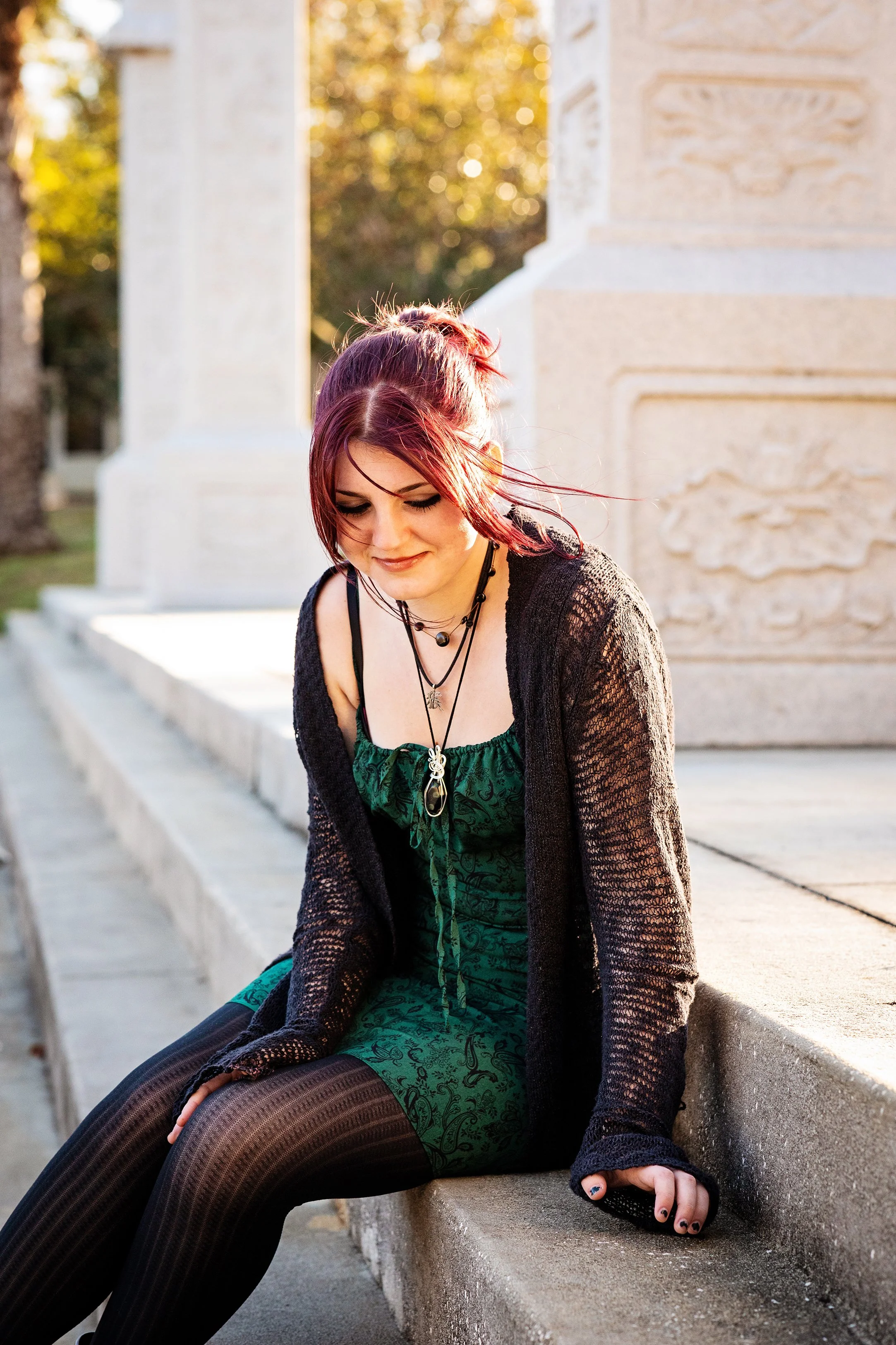 Lifestyle portrait of a red-haired woman with tattoos seated on a stone ledge outdoors, photographed by Lindsay Parks Photography