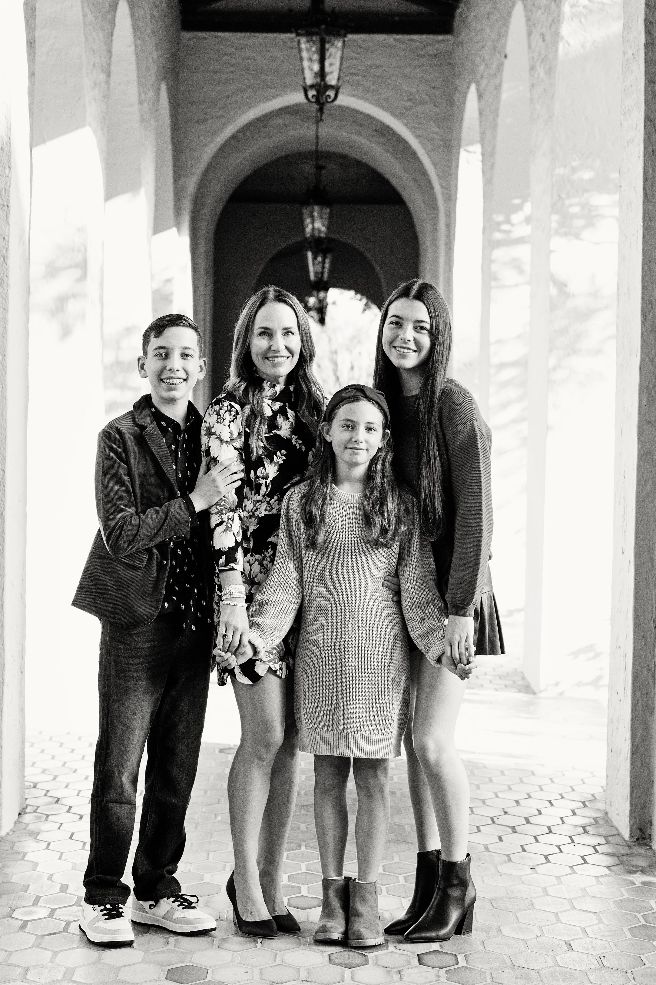 Black and white extended family portrait of five people holding hands beneath an arched walkway with lanterns with gorgeous natural light.