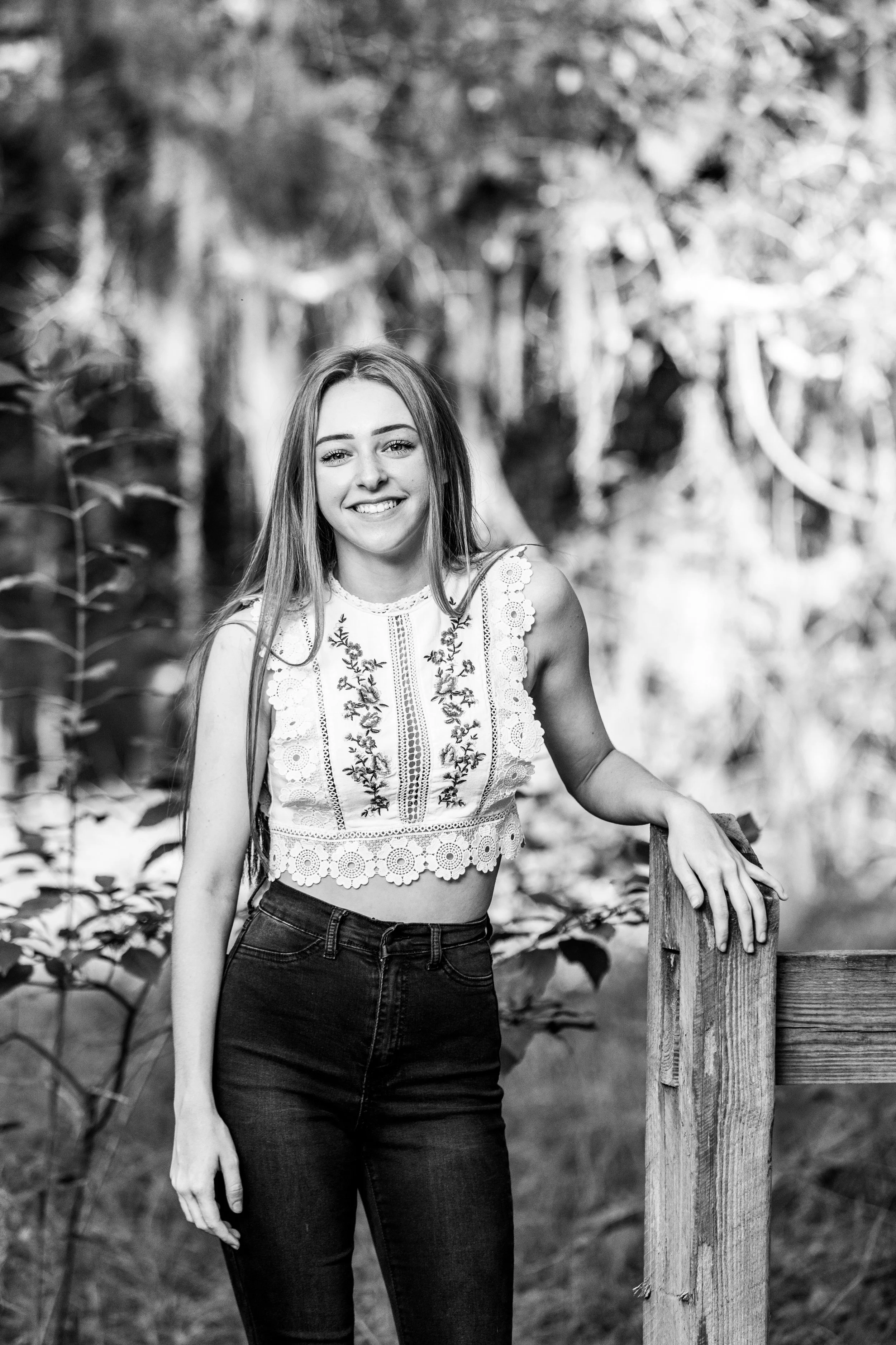 Outdoor lifestyle portrait of a young woman standing beside a wooden post in a natural setting, photographed by Lindsay Parks Photography