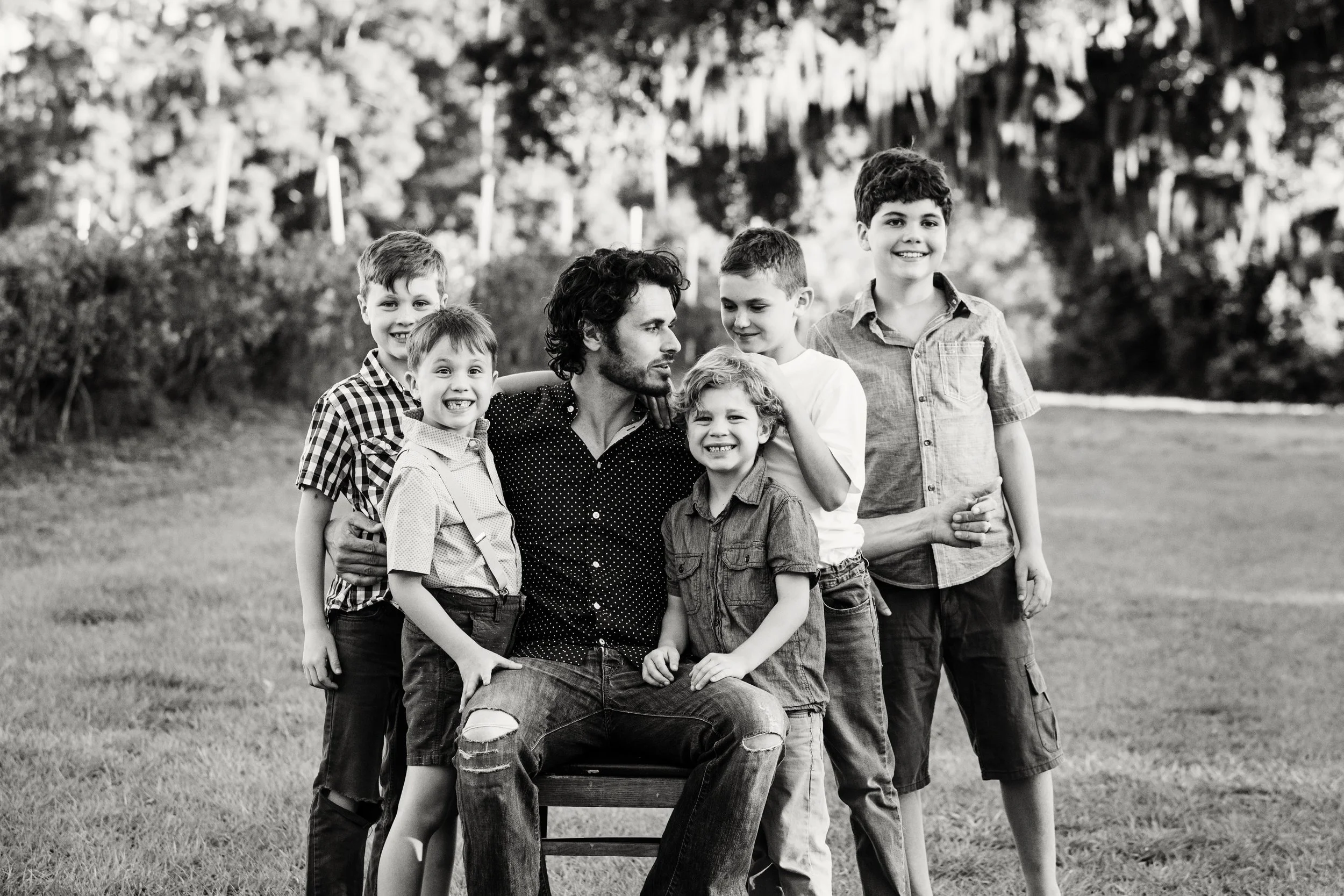Black and white lifestyle portrait of a man surrounded by six boys in a Florida park setting using natural light. 