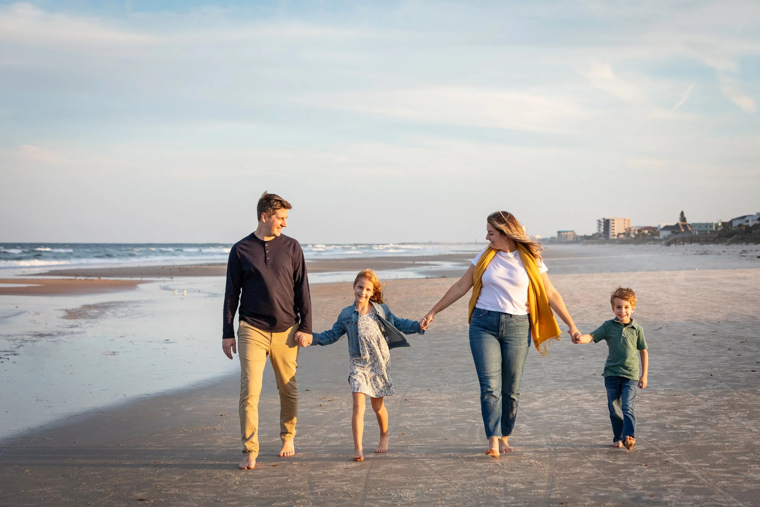 Florida beach family photography of parents and children walking hand in hand at sunset under a clear sky.