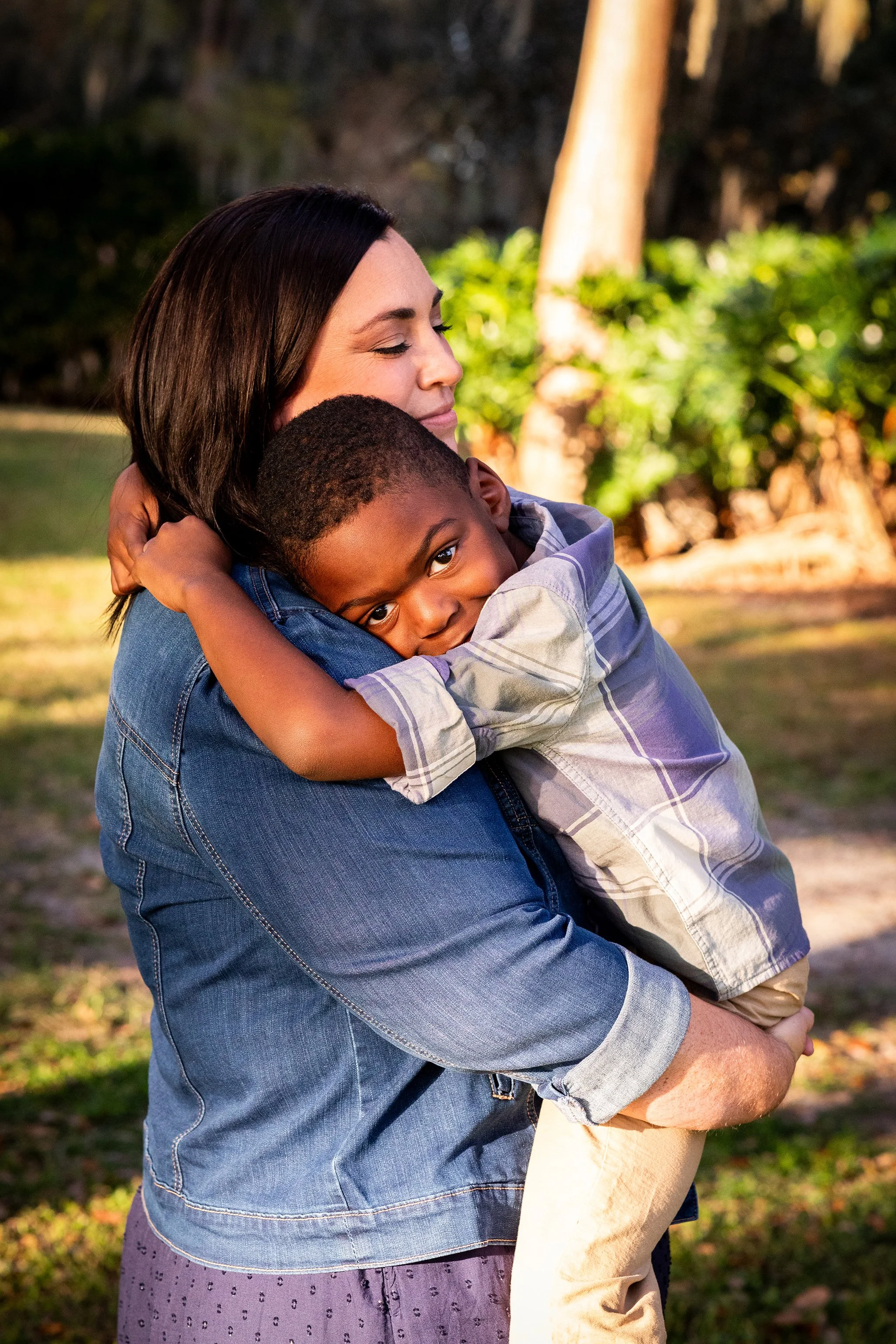 Lifestyle family portrait of a mother hugging her young son outdoors among trees