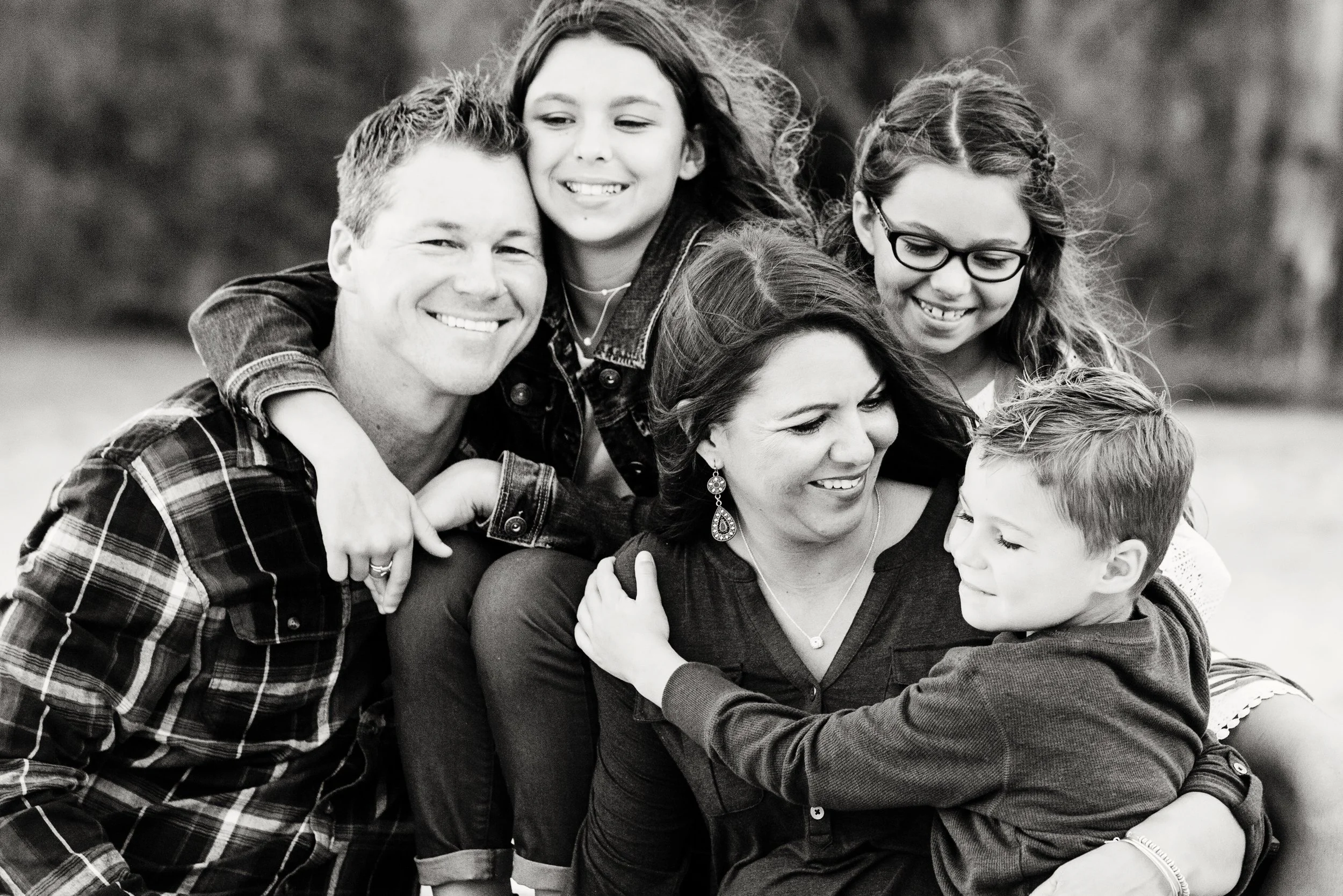 Black and white extended family photography of six people hugging and smiling outdoors