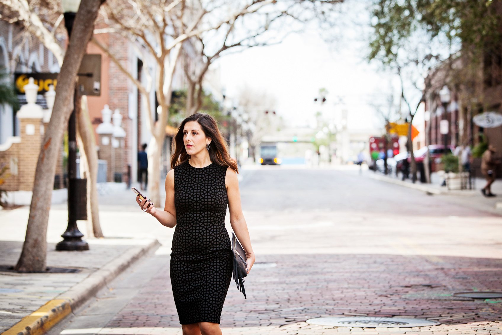 Urban lifestyle portrait of a woman walking along a city sidewalk while looking at her phone
