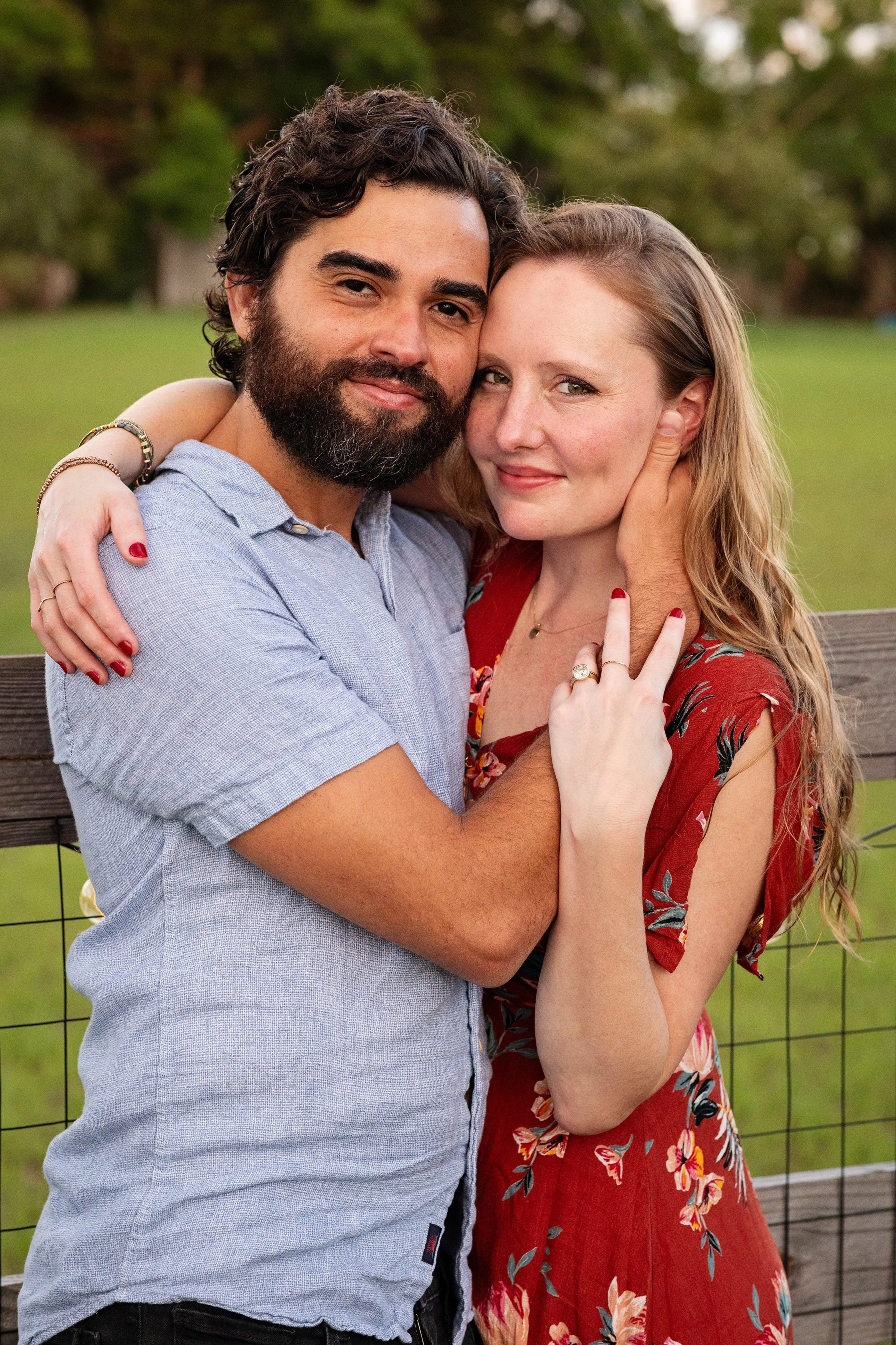 Lifestyle couple portrait of a couple hugging outdoors near trees and a fence at sunset.