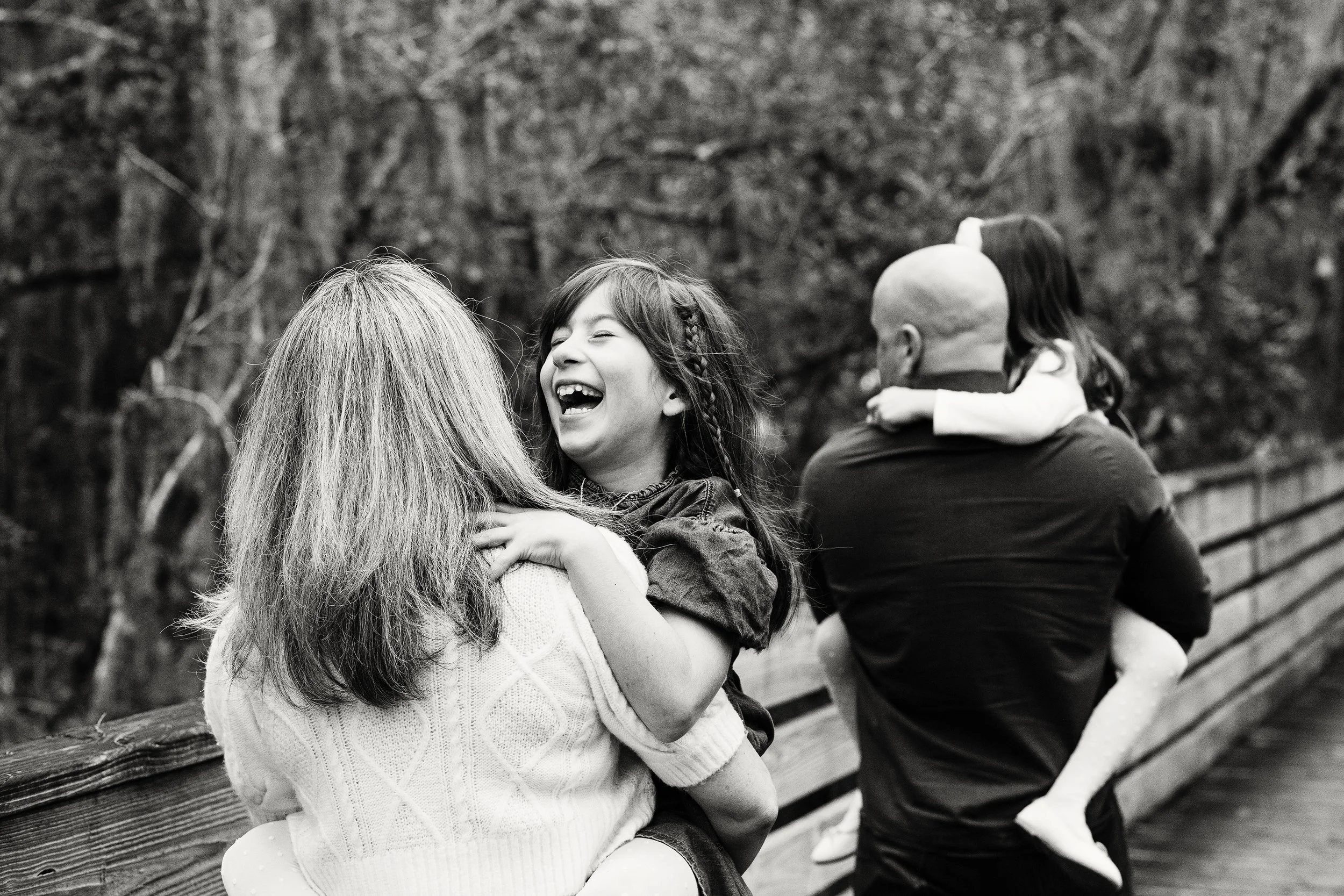 Lifestyle family photography of parents and daughters laughing together on a wooden bridge