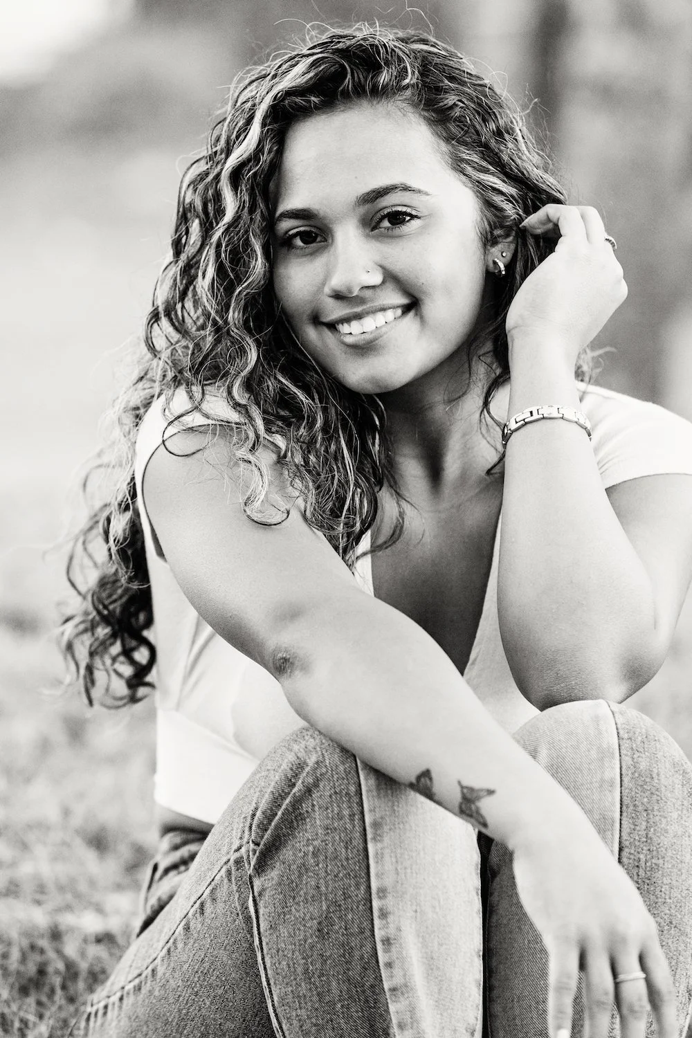 Black-and-white lifestyle portrait photo of a smiling young woman with curly hair outdoors, photographed by Lindsay Parks Photography