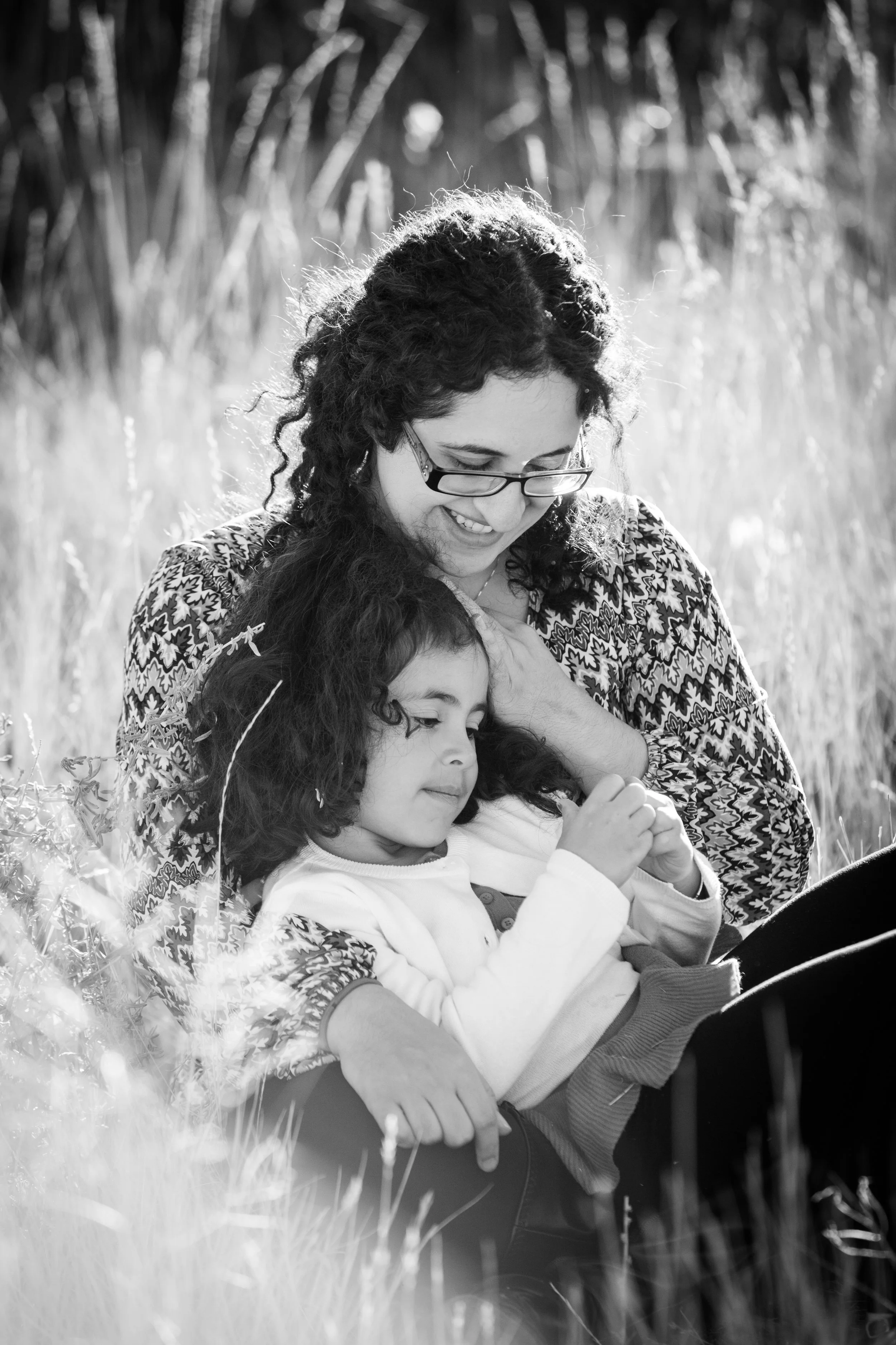 Black and white lifestyle family portrait of a mother and two daughters sitting together in tall grass