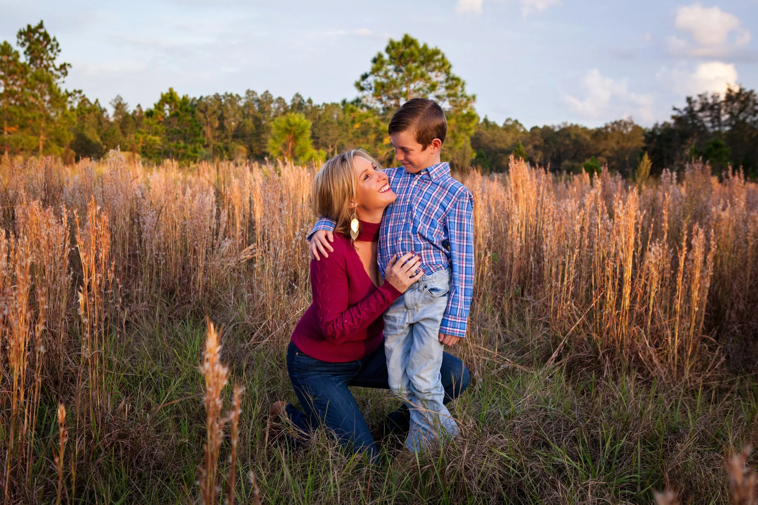 Golden hour family photography of a mother kneeling in tall grass hugging her young son