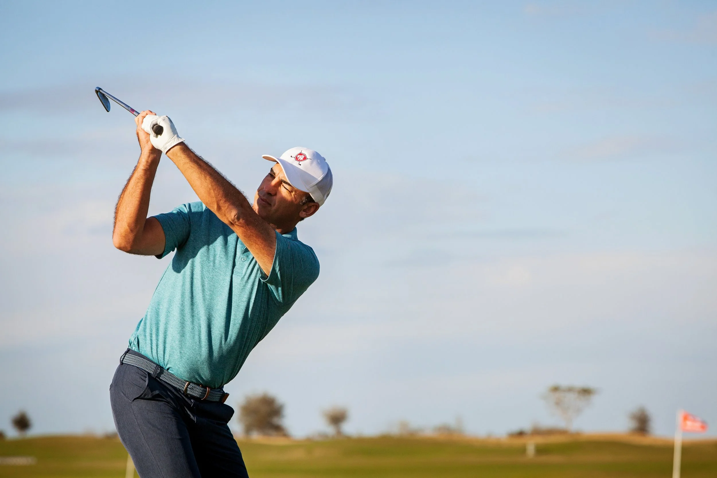 Sports action photography of a man swinging a golf club on a course during daytime