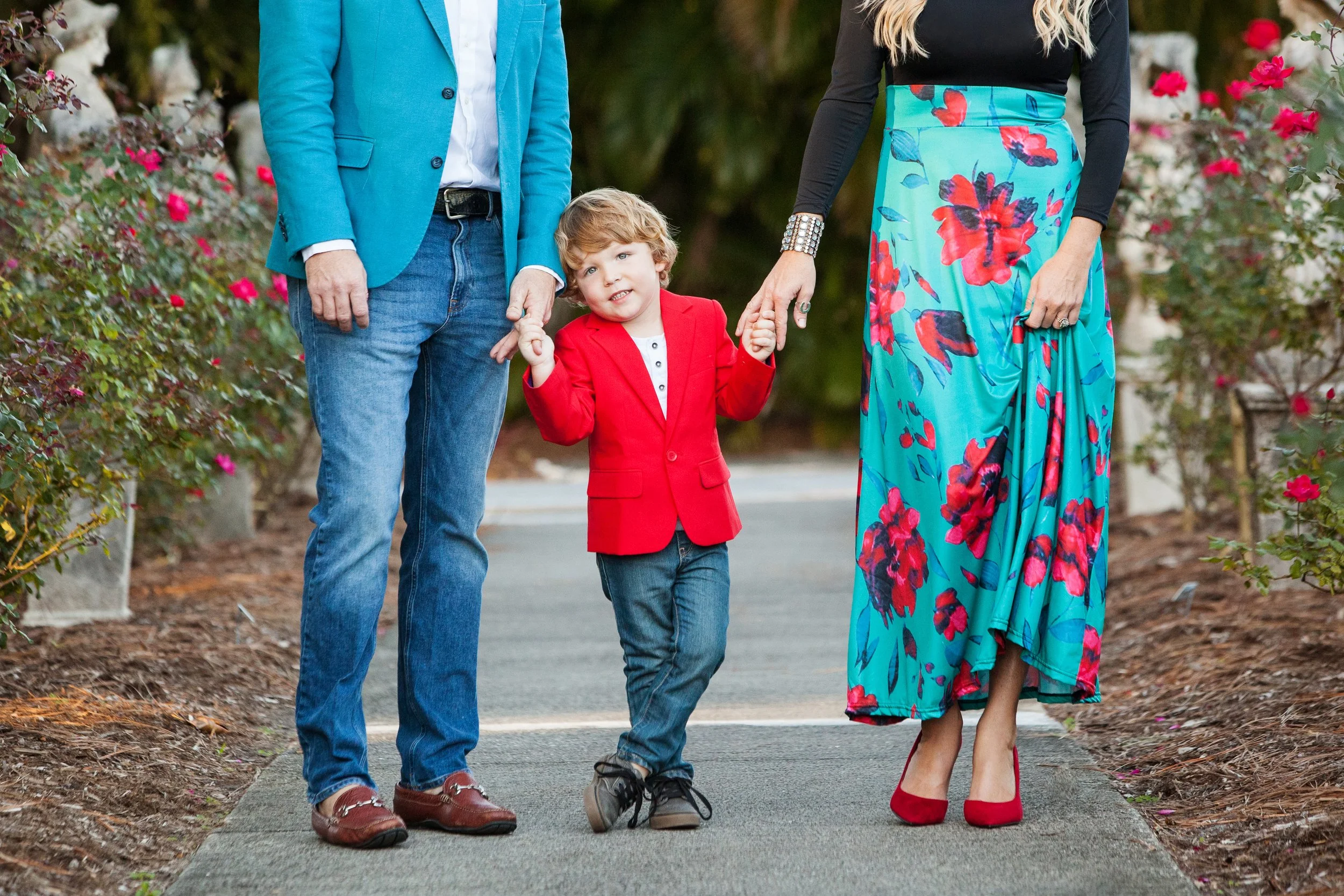 Lifestyle family portrait of parents and child holding hands while walking through a garden path