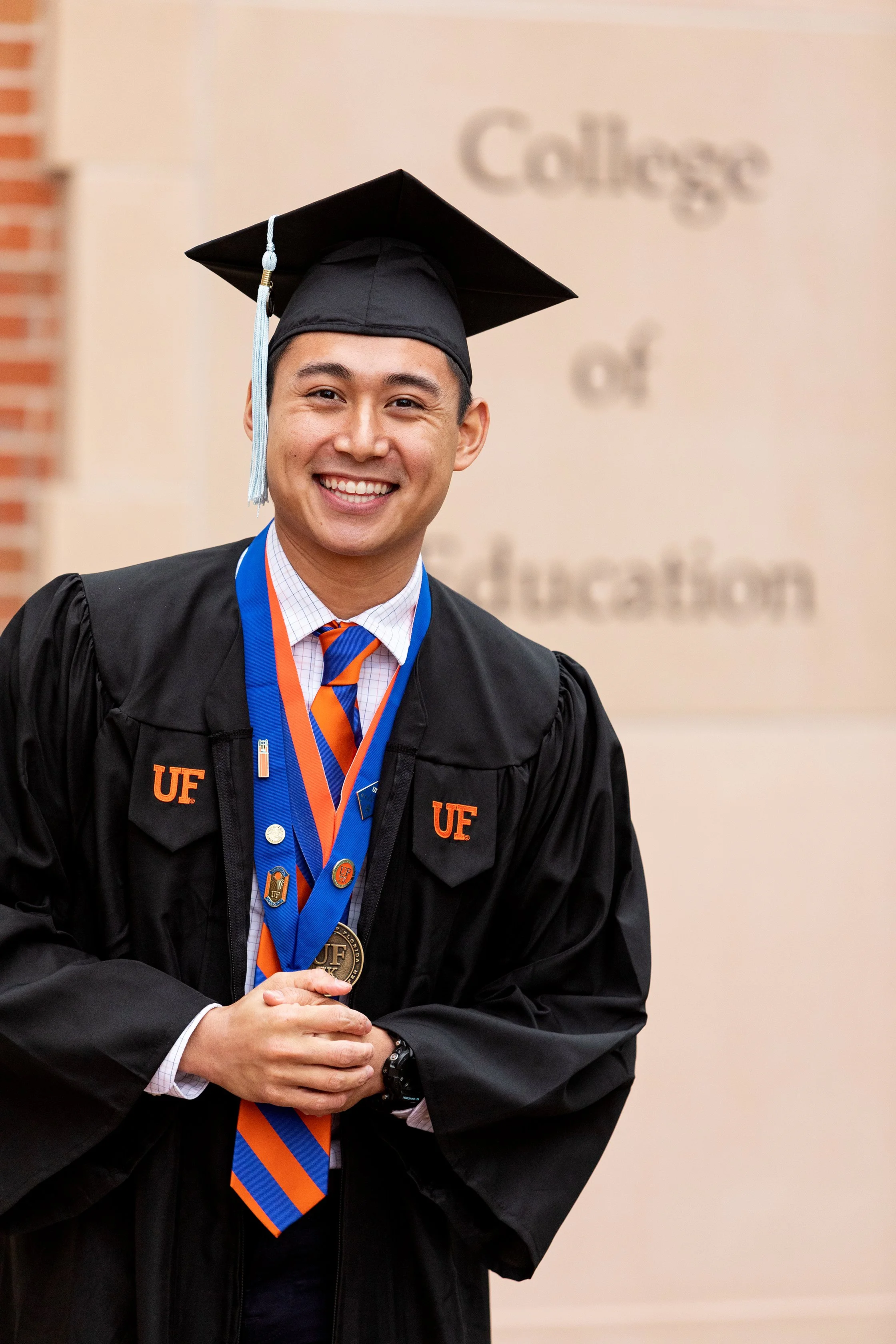 High school graduation portrait photography of a male graduate in cap and gown with medals outside the College of Education, photographed by Lindsay Parks Photography.