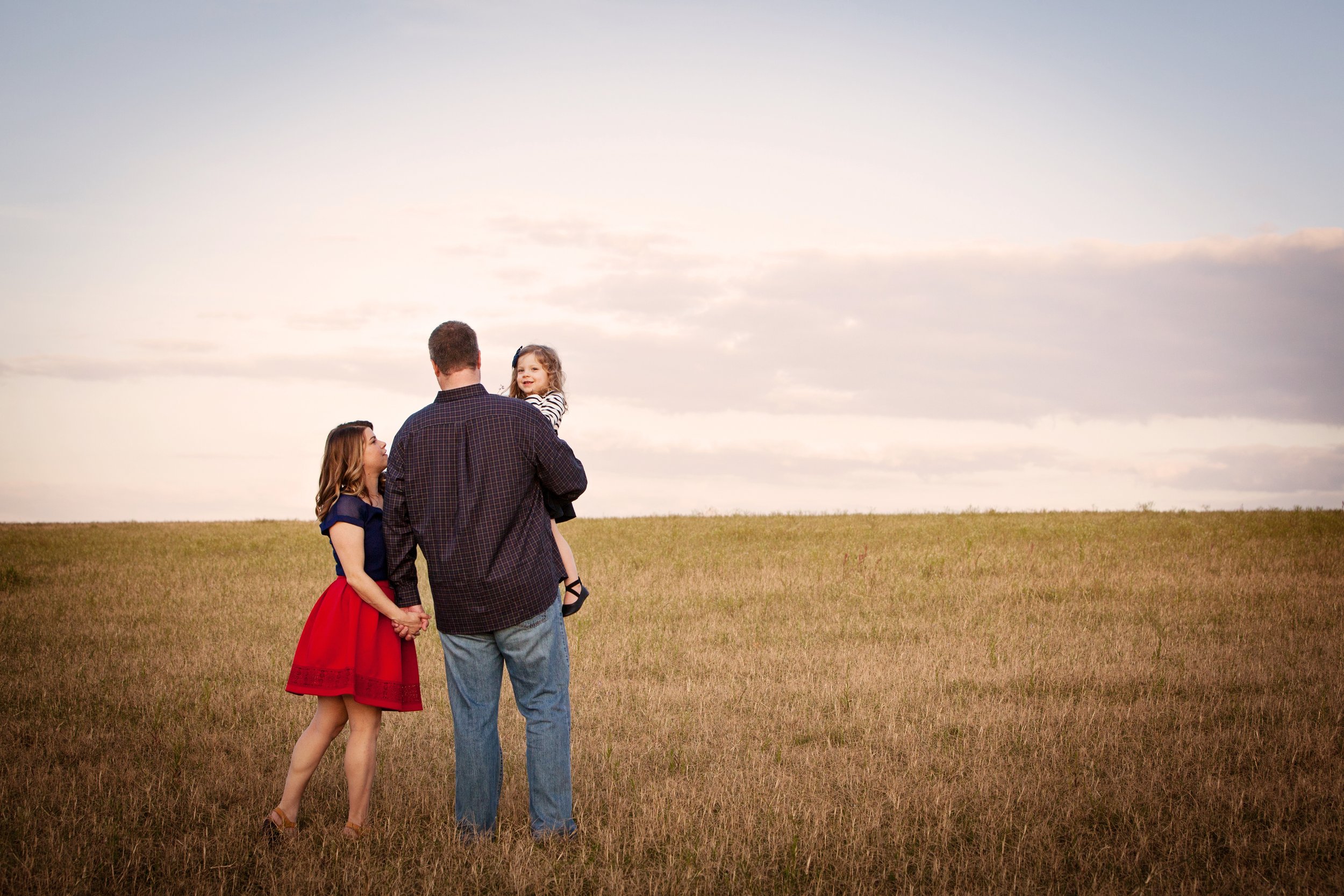 Outdoor family photography of parents and daughter standing together in an open field during a clear Floriday day.