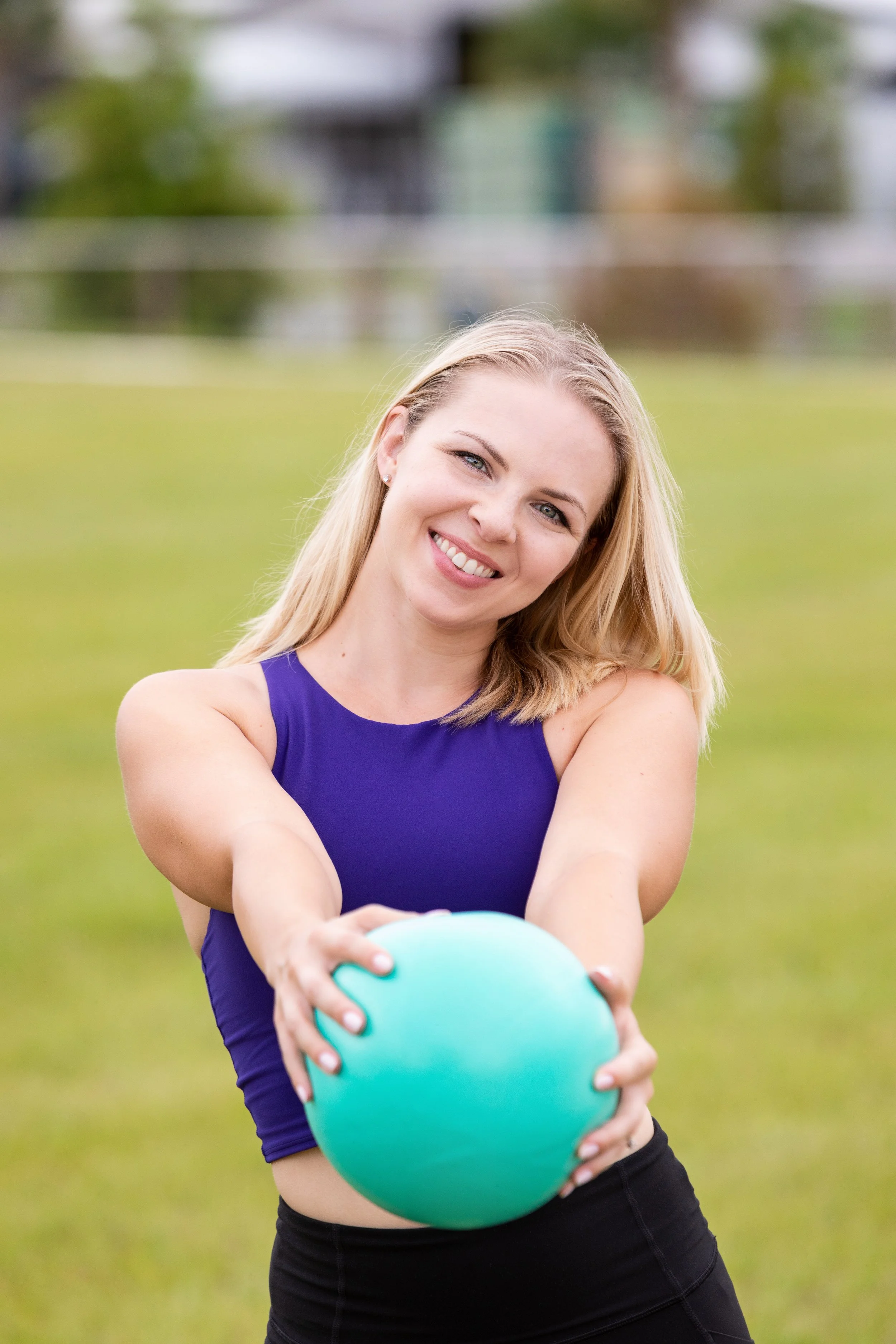 Lifestyle fitness portrait of a woman smiling while holding an exercise ball outdoors and smiling lightheartedly.