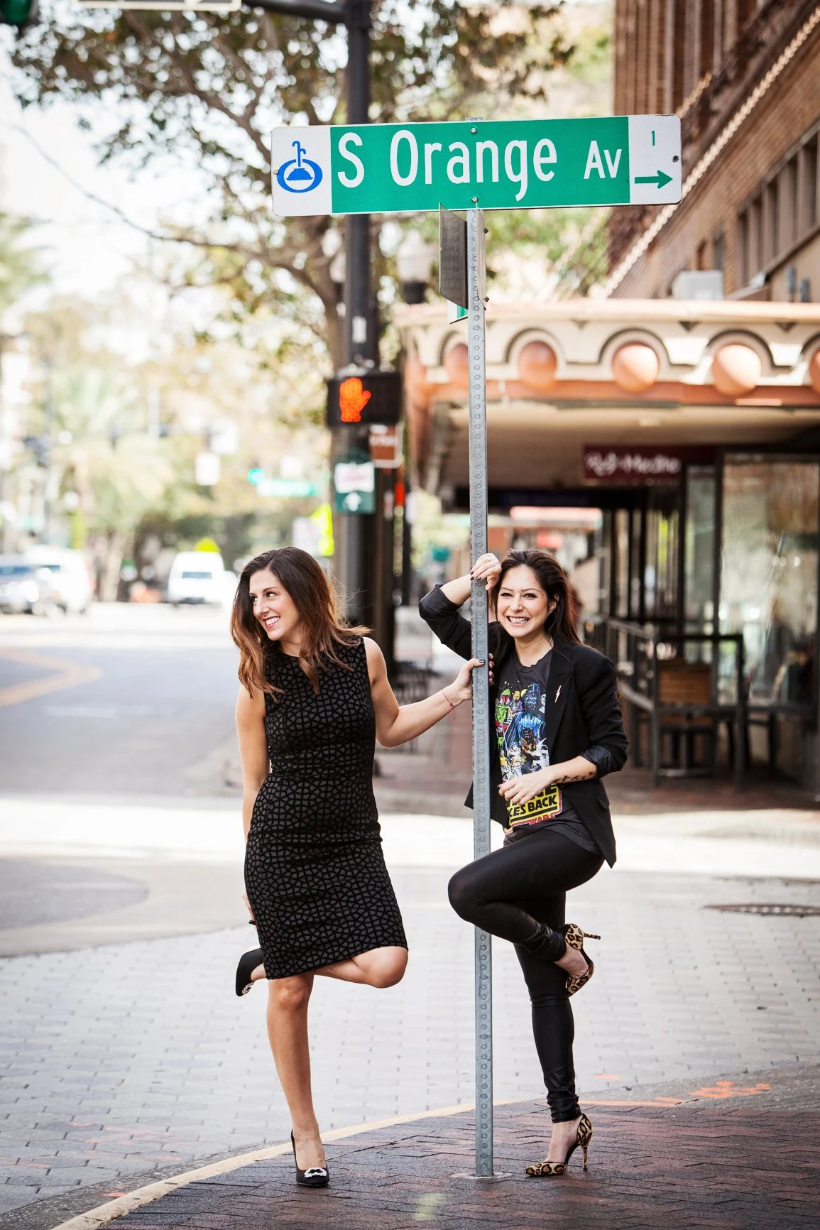 Lifestyle branding photography of women standing on a sidewalk next to a street sign reading' S Orange Ave' with an accessibility symbol. They are smiling and posing playfully.