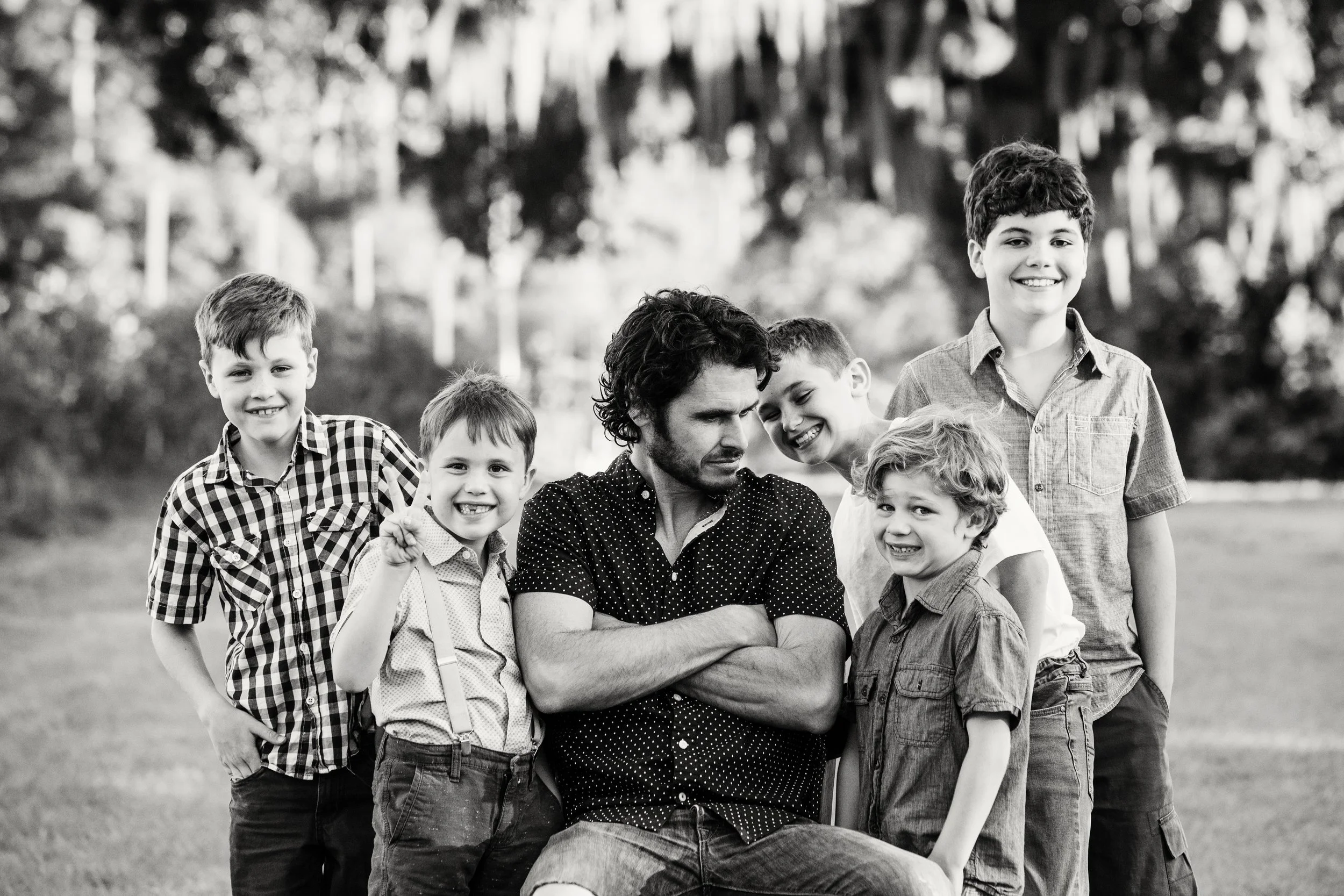Black and white lifestyle portrait of a man seated outdoors surrounded by six boys