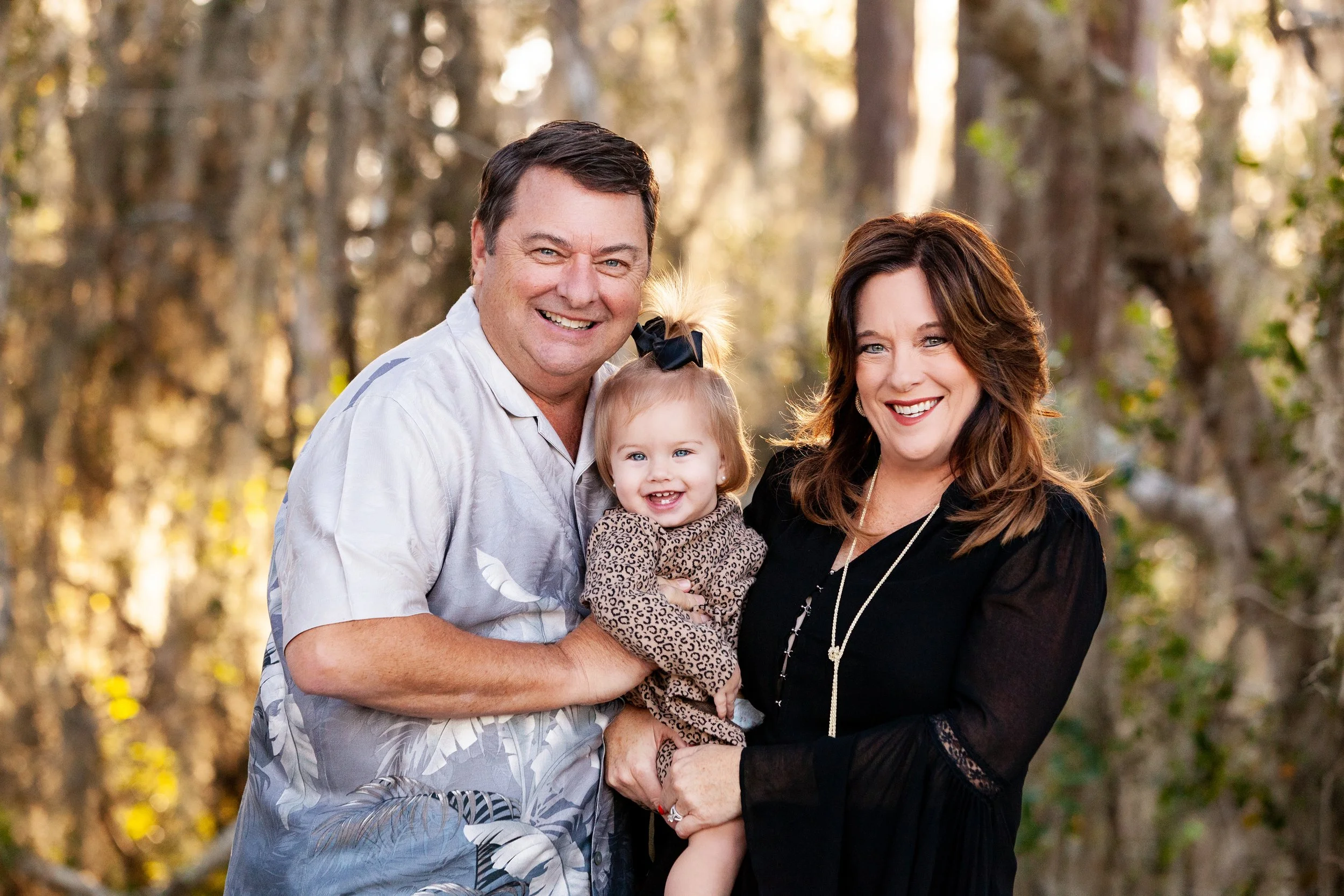 Outdoor family portrait of parents and young daughter smiling together in a wooded setting