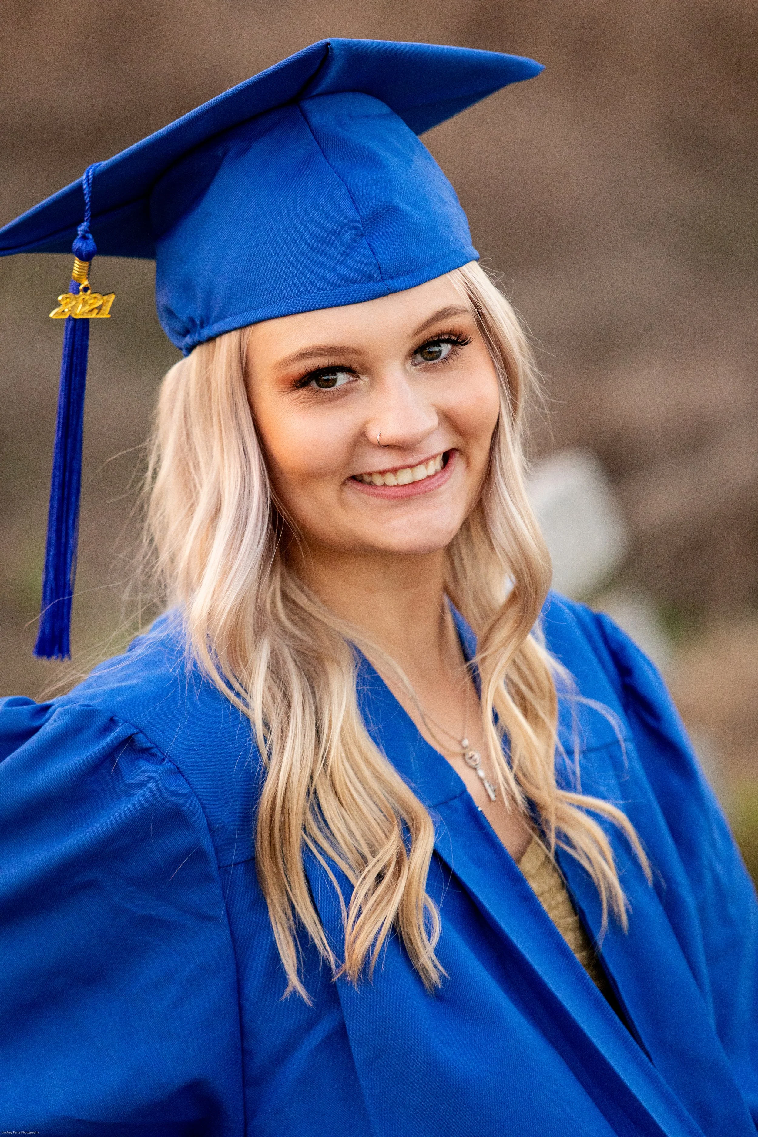 Senior graduation portrait of a young woman in a blue cap and gown smiling outdoors
