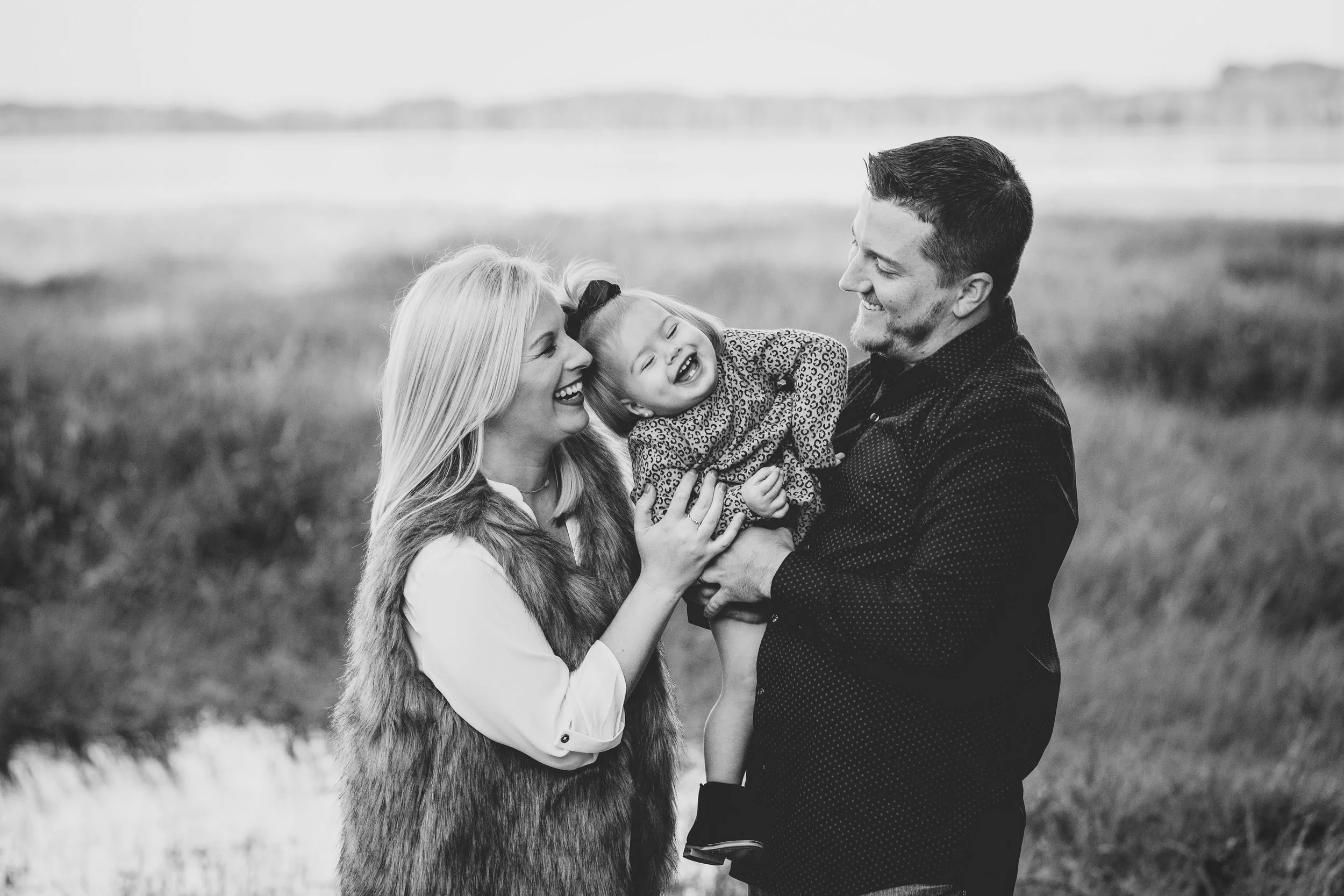 Outdoor family photography of parents and daughter playing together in an open field. Black and white photograph using the natural light to enhance the happy family.
