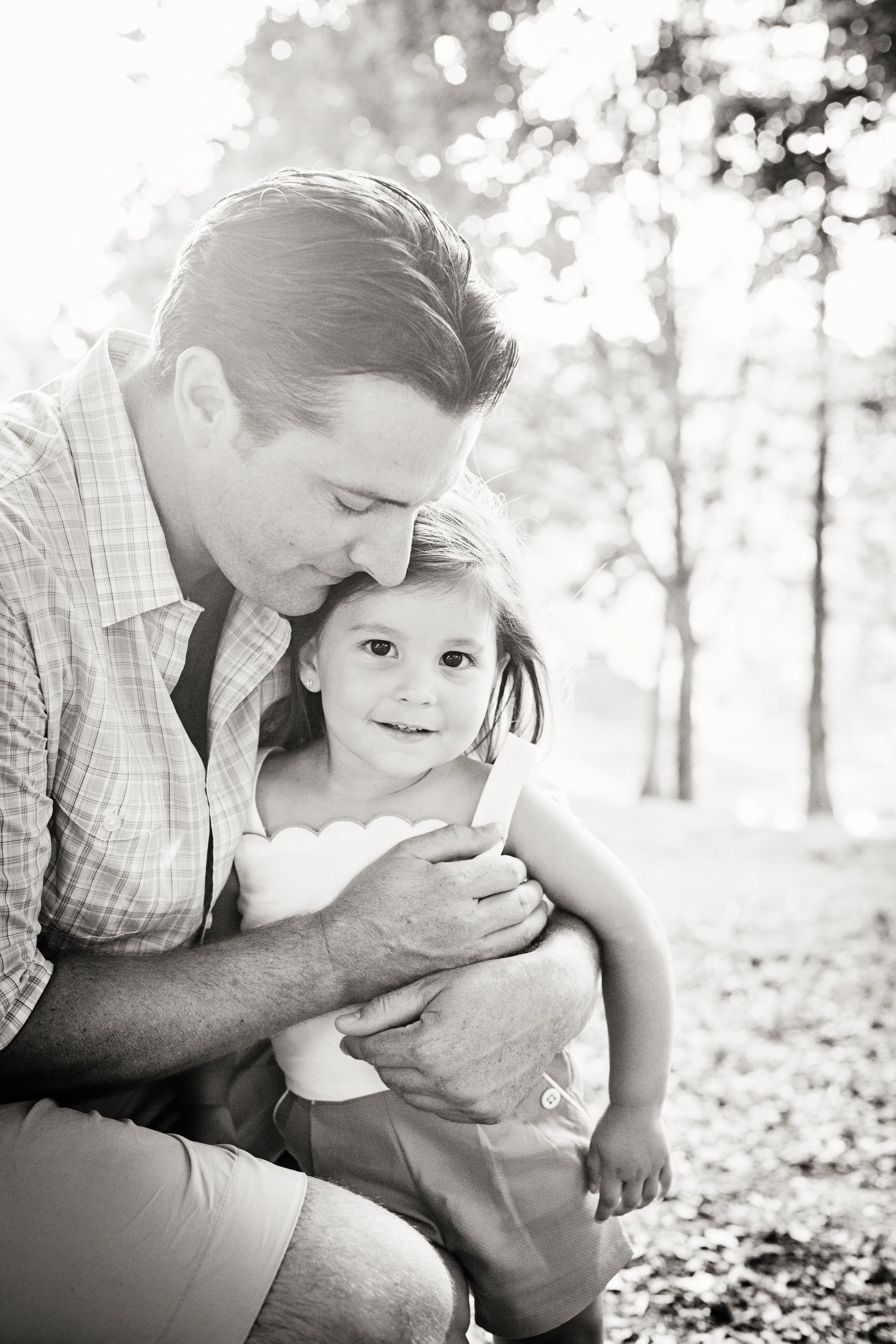 Black and white family photography of a father hugging his young daughter outdoors