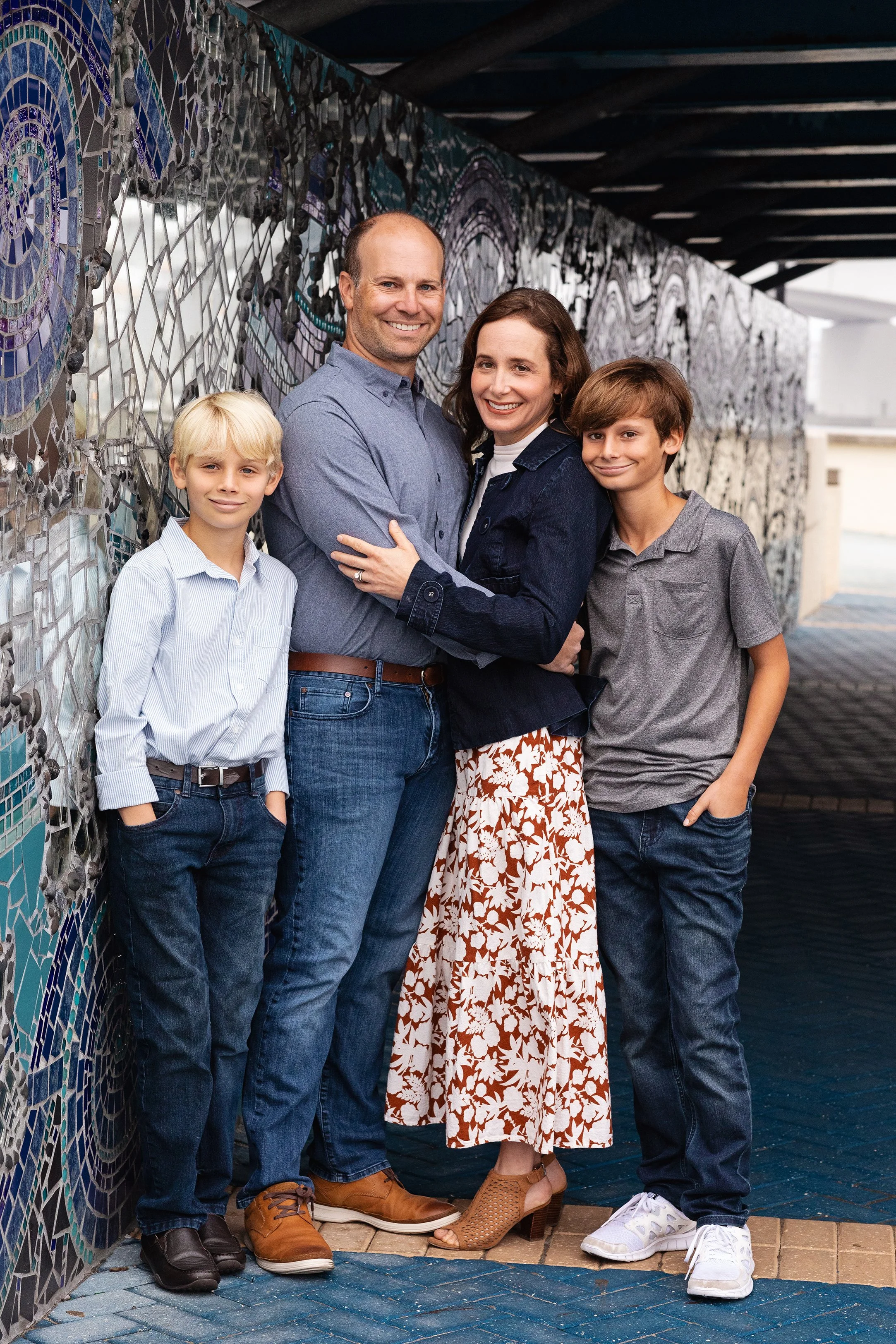 Extended family portrait of five people hugging together in front of a mosaic wall taken by Lindsay Parks Photography.