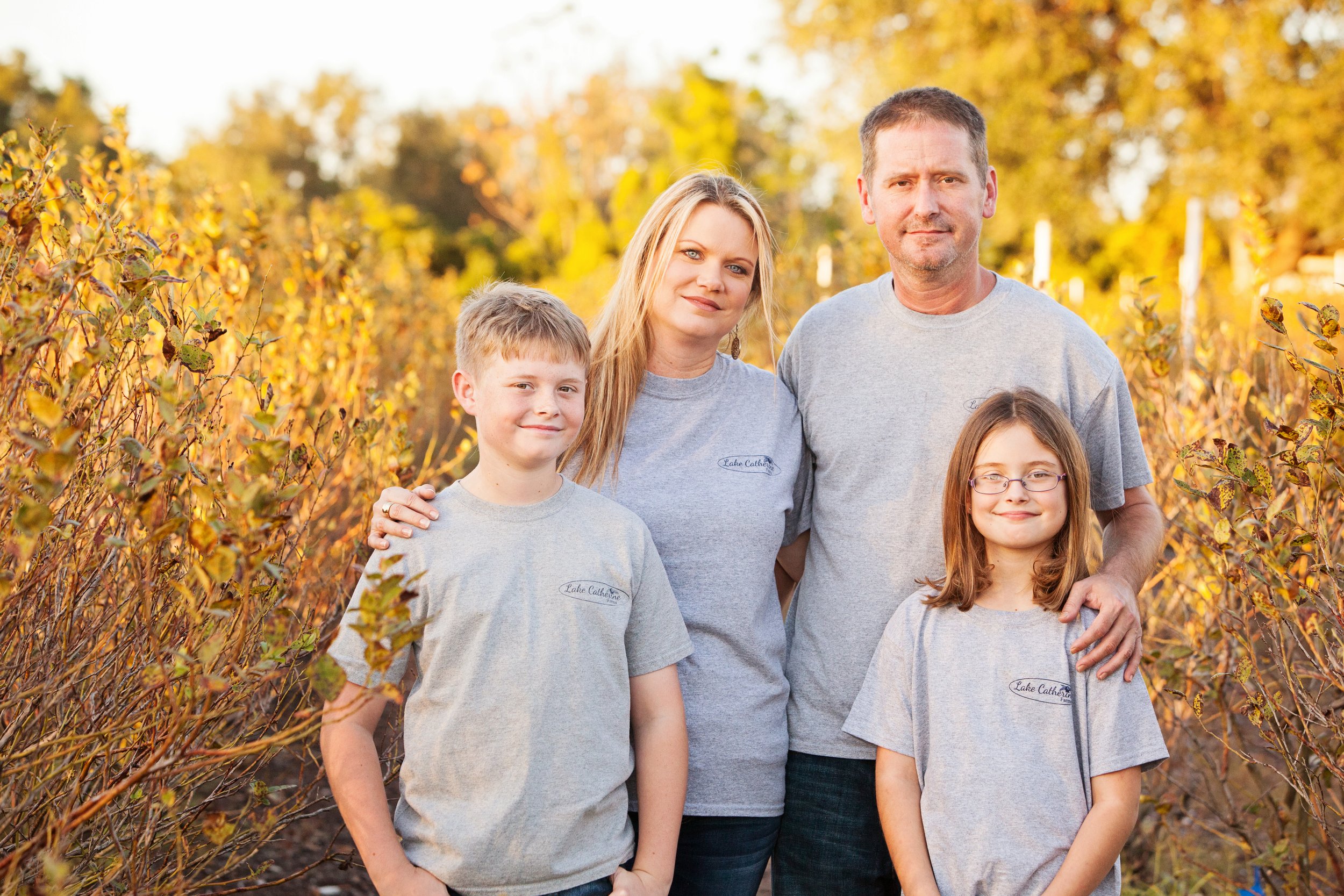 Fall family photography of a family of four wearing matching shirts surrounded by autumn leaves at golden hour.