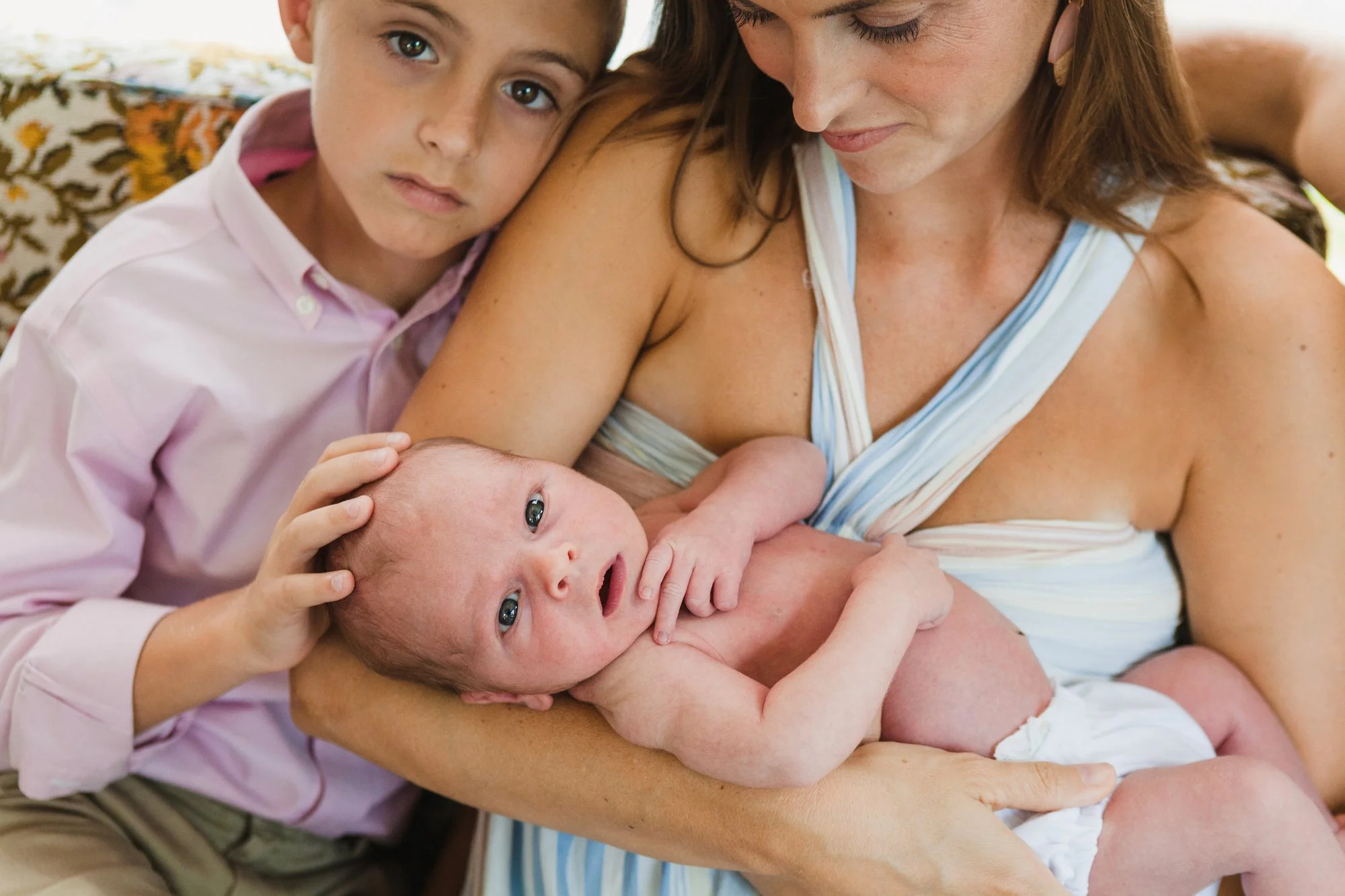 Lifestyle newborn portait photography of a mother holding her newborn while an older child gently cuddles beside her, photographed by Lindsay Parks Photography.