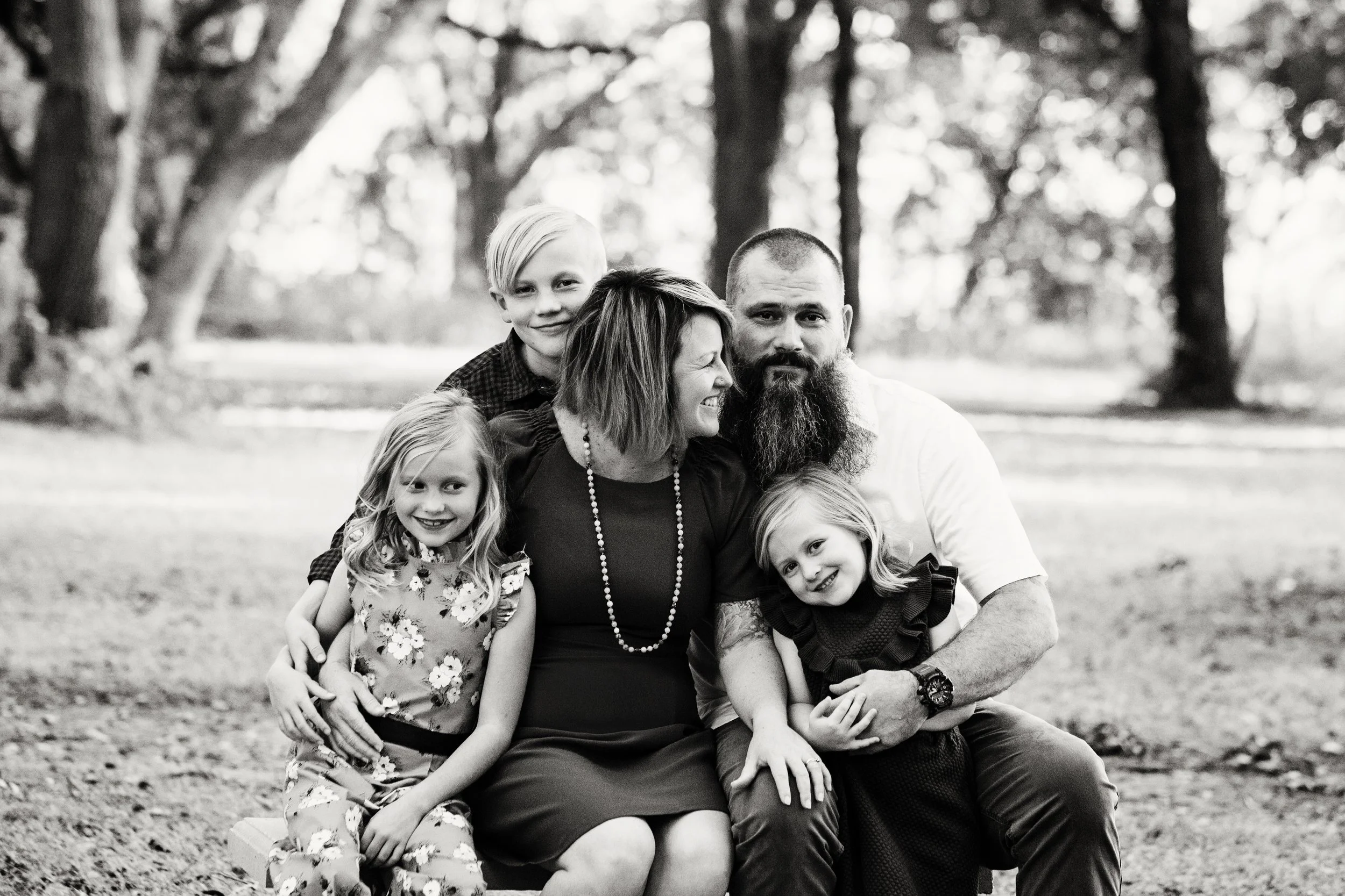 Black and white family photography of parents and four daughters cuddling on a bench. 
